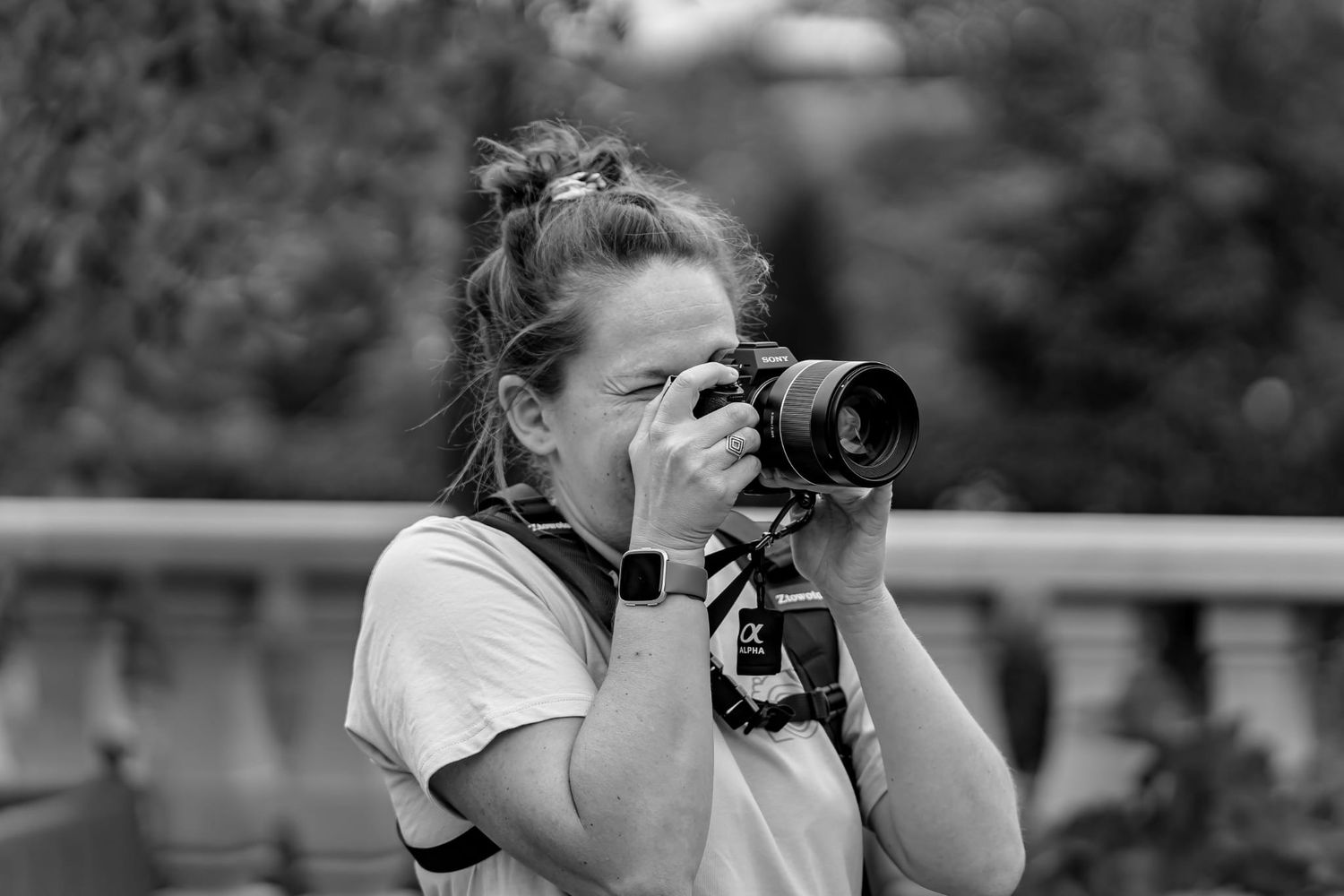 A photographer in a white t-shirt takes pictures using a professional camera on a railing in black and white.
