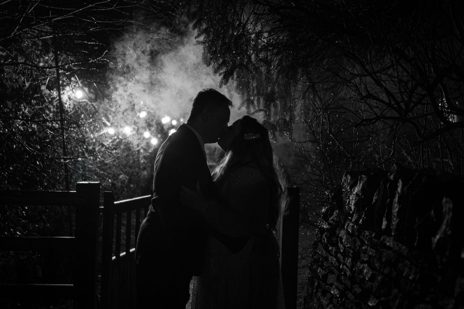 A romantic silhouette of a couple kissing at night with fireworks illuminating the dark winter sky in the background.