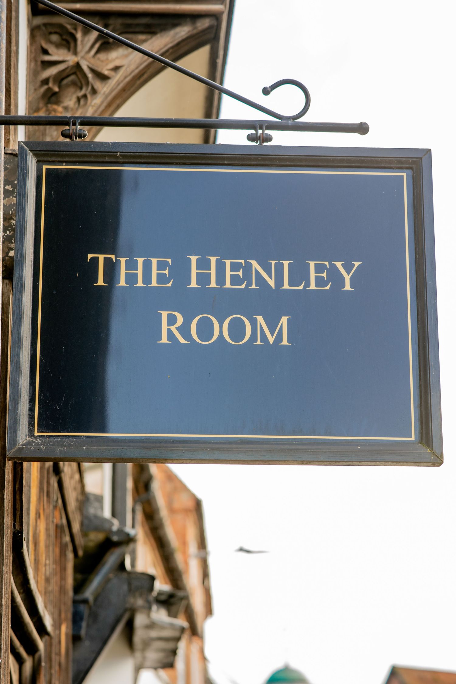 A hanging black sign with gold lettering reading 'The Henley Room' mounted on a brick building exterior.