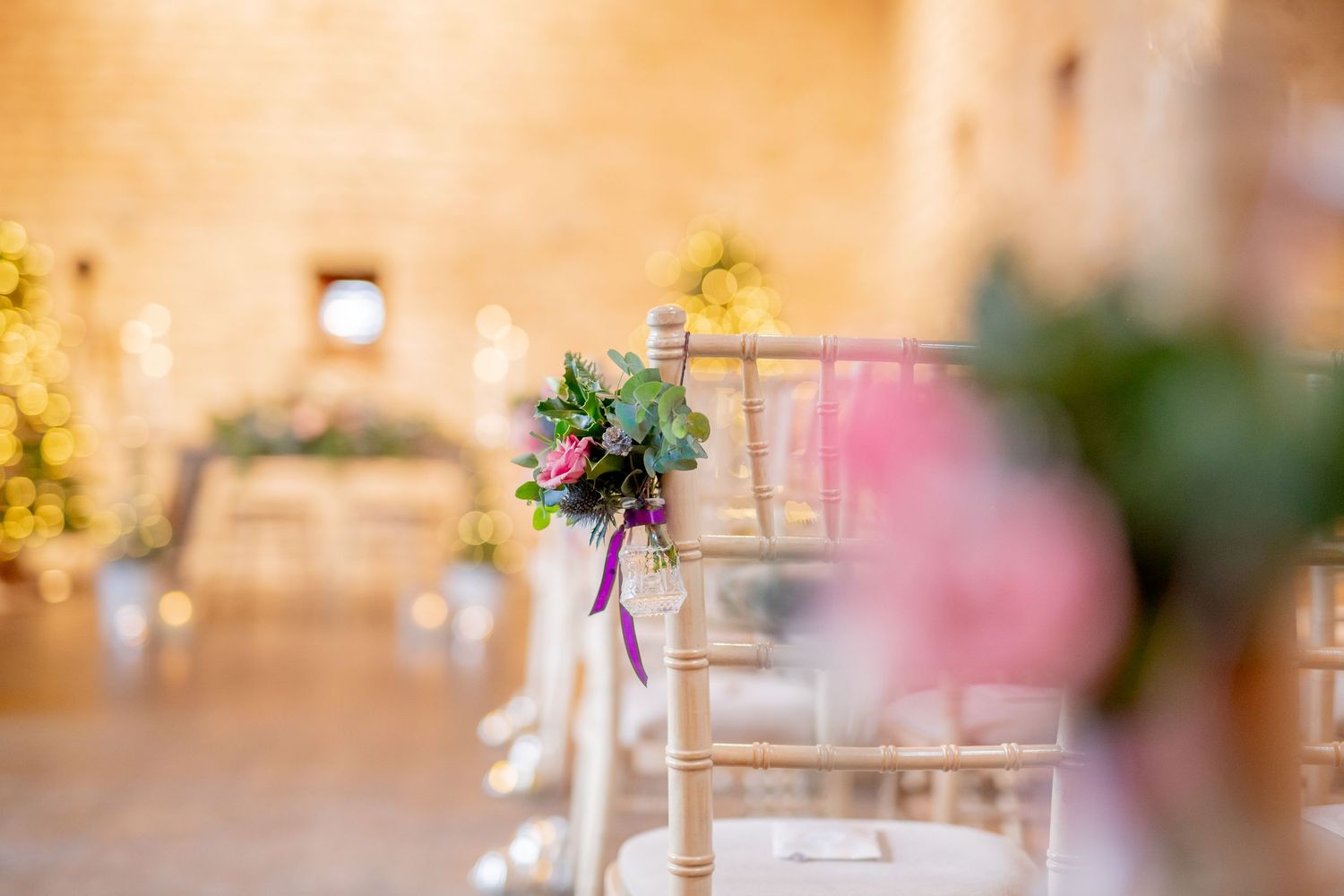 Elegant chair decorations with purple flowers at a wedding venue are shown in soft focus detail.
