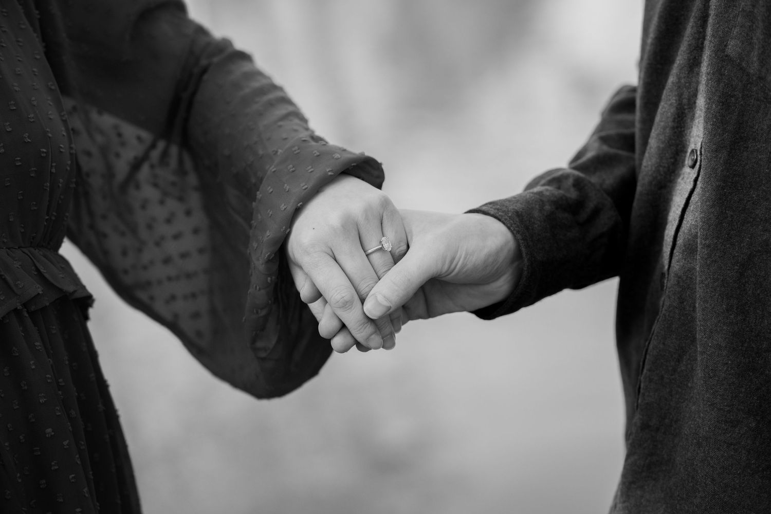 A black and white close-up photograph of two people holding hands together in an intimate moment.