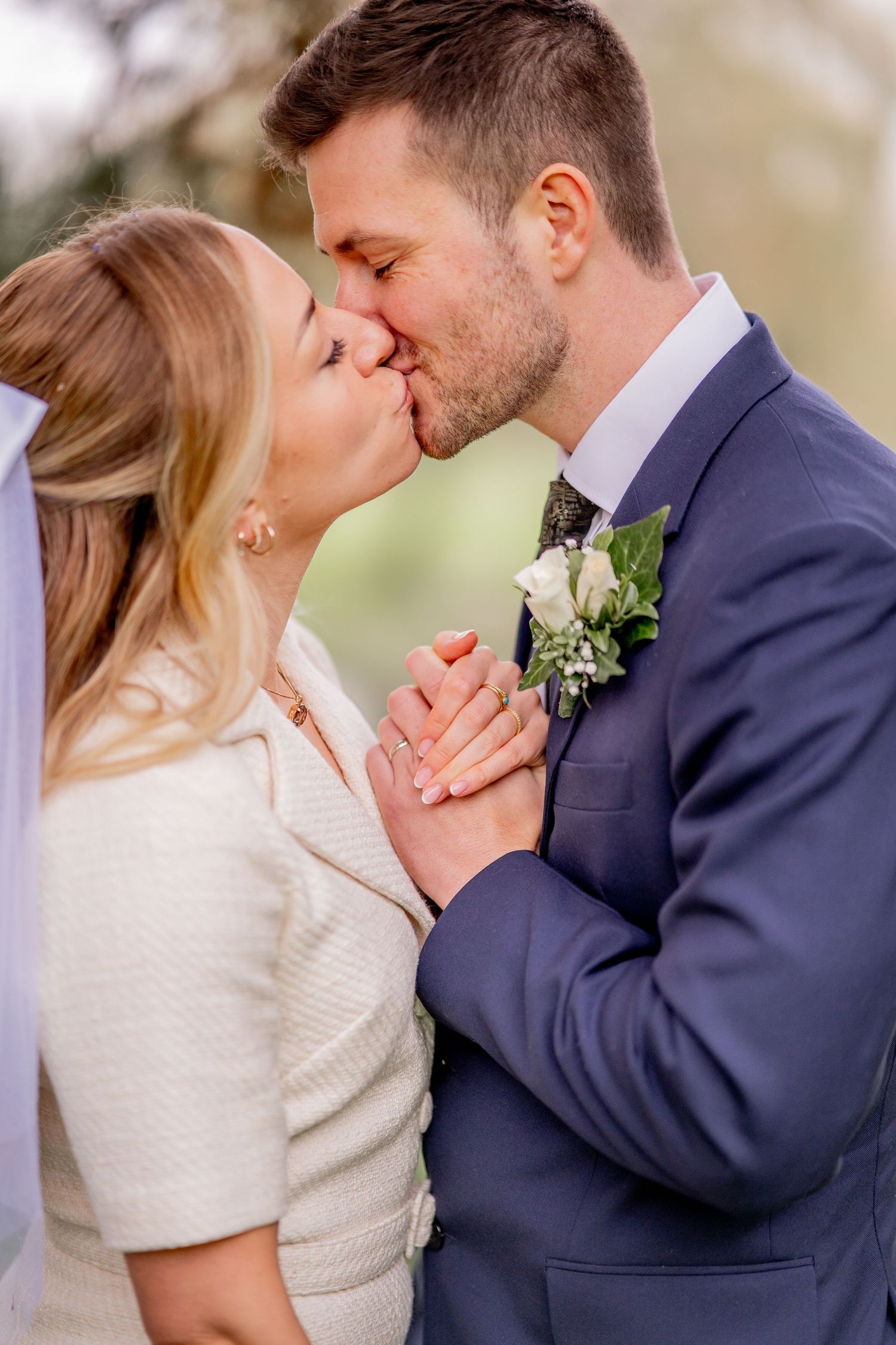 Romantic wedding photograph showing a tender kiss between newlyweds, with the groom wearing a navy suit and white boutonniere.