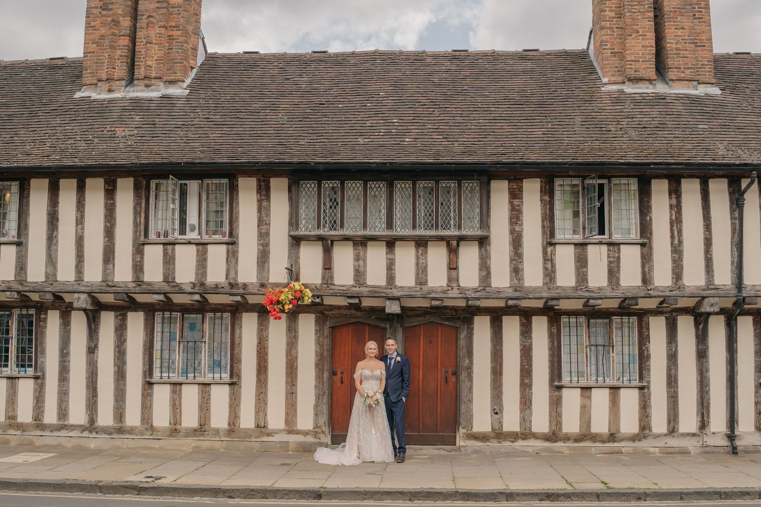 Bride and groom posing before a historic Tudor timber-framed building on their wedding day.
