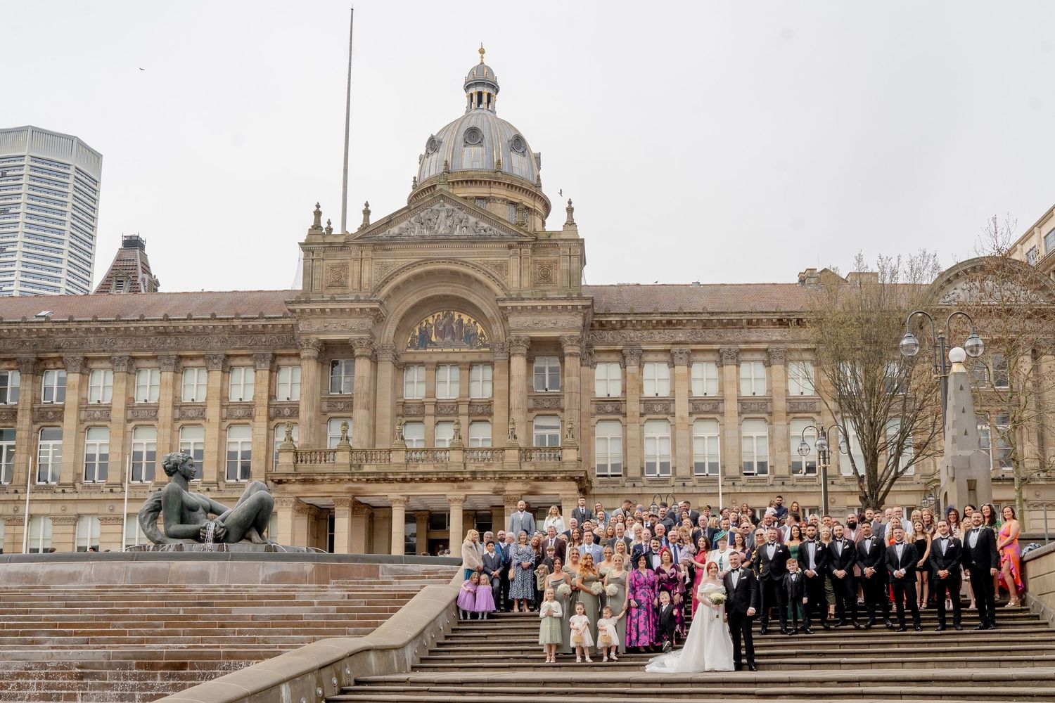 Large wedding party gathered on the steps of Birmingham Council House with its ornate Victorian architecture and domed tower.