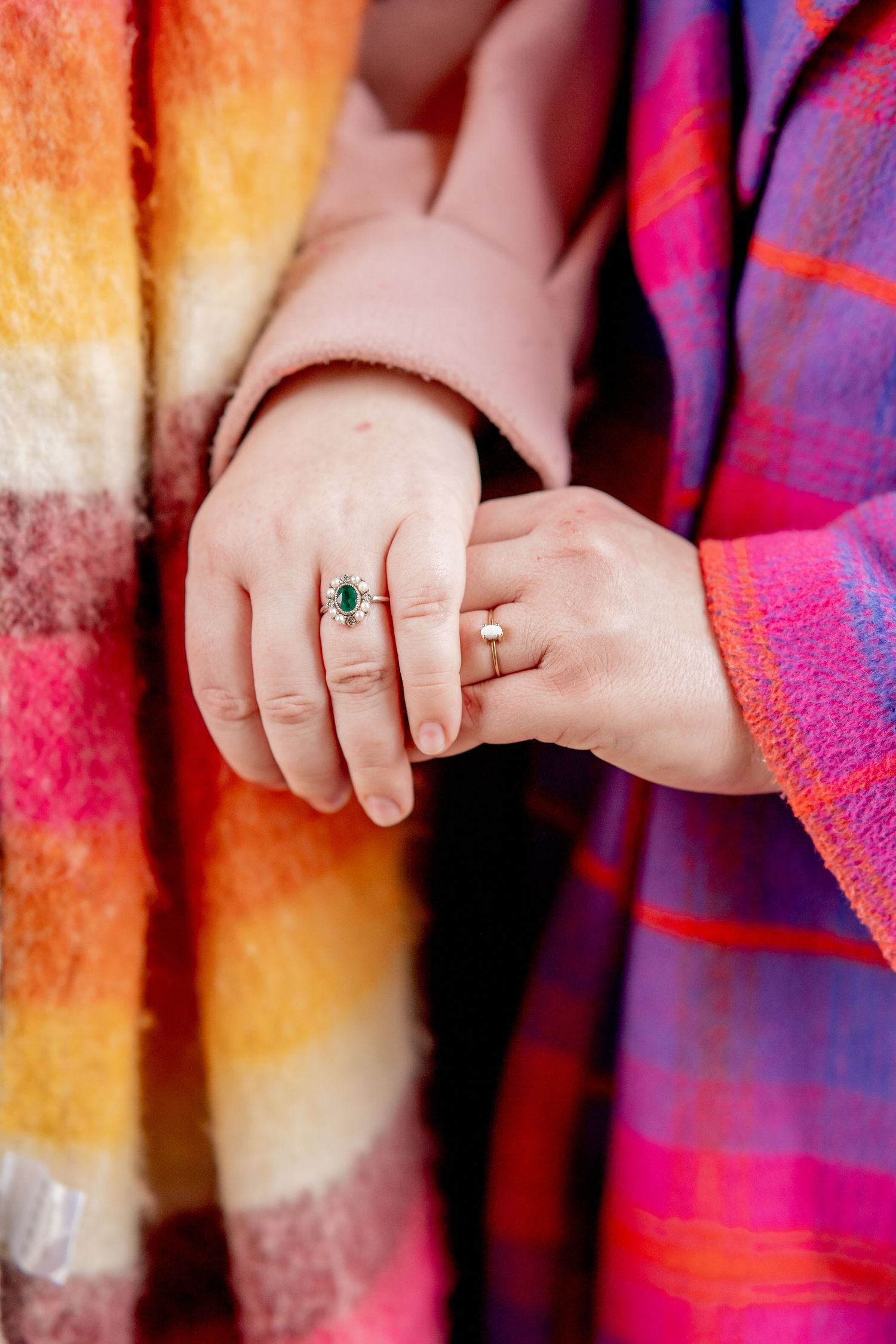 Close-up of hands wearing an emerald ring against colorful plaid and striped blanket backgrounds.
