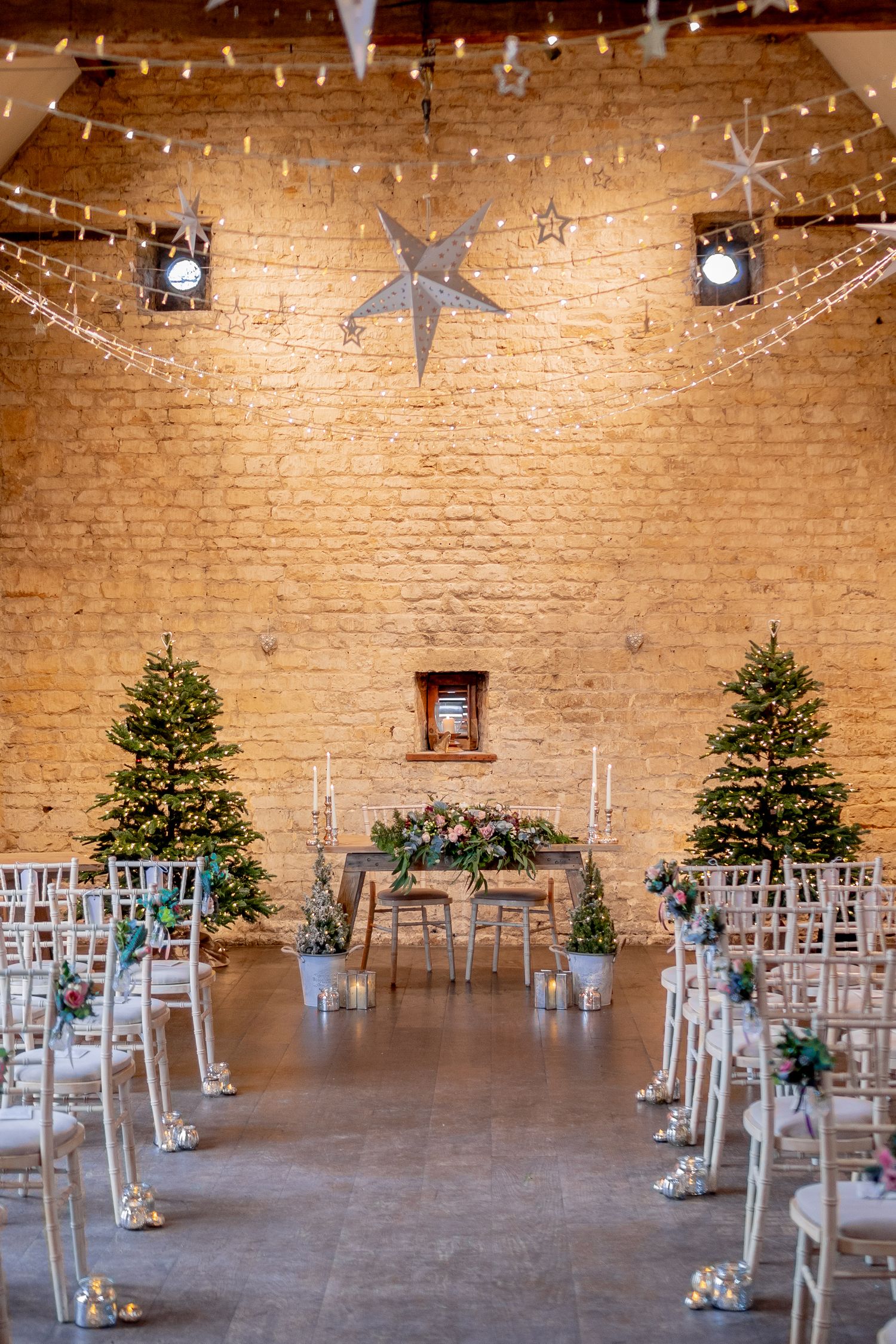 Wedding ceremony venue with exposed brick walls, twinkling string lights, silver star decor and two Christmas trees.