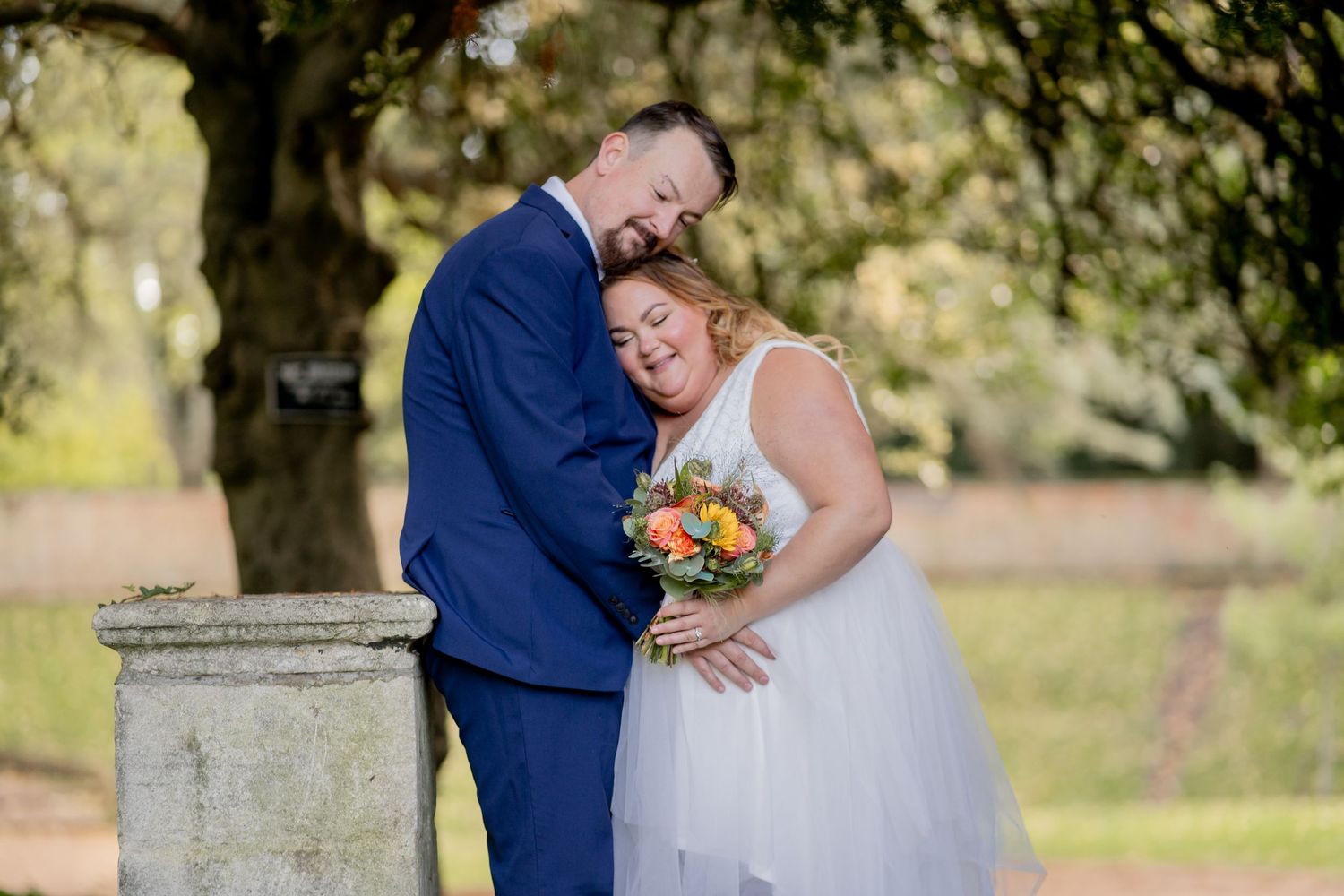 A couple shares an intimate moment outdoors during their wedding, with the bride holding a colorful bouquet.