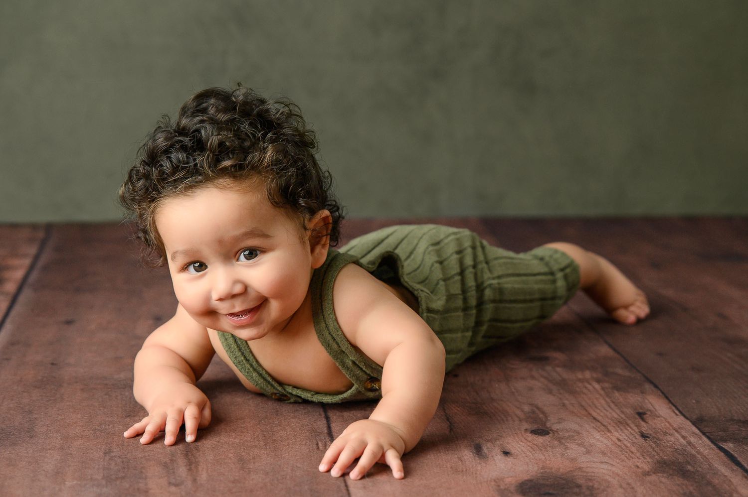 Series of artistic baby photos on dark wooden floor with olive green outfit.