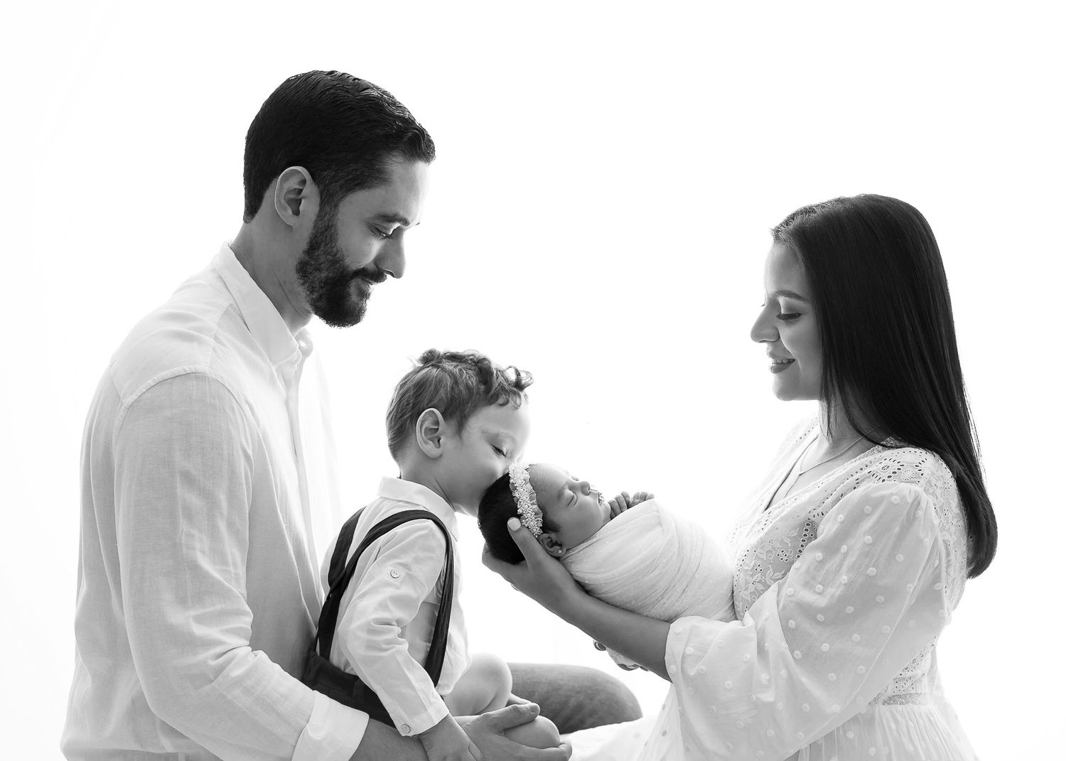 Black and white family portrait with parents and two young children against a white background.