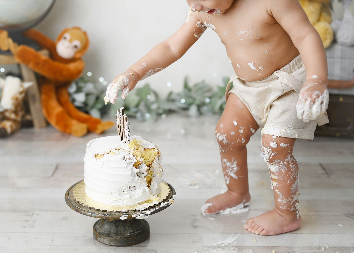 Small cake smash photo with messy frosting and tiny feet covered in white icing.