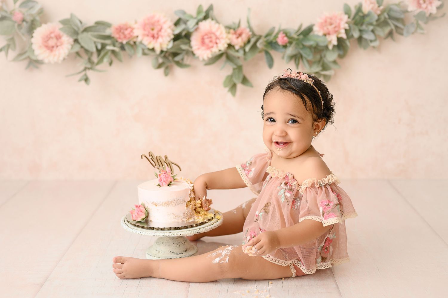 Cake smash photo session with pink floral decorations and vintage styling.
