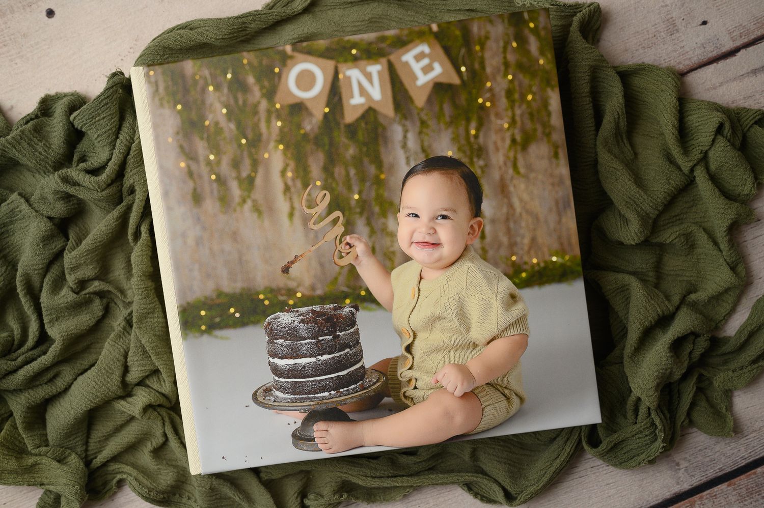 First birthday cake smash session with green drapery and rustic wooden elements.