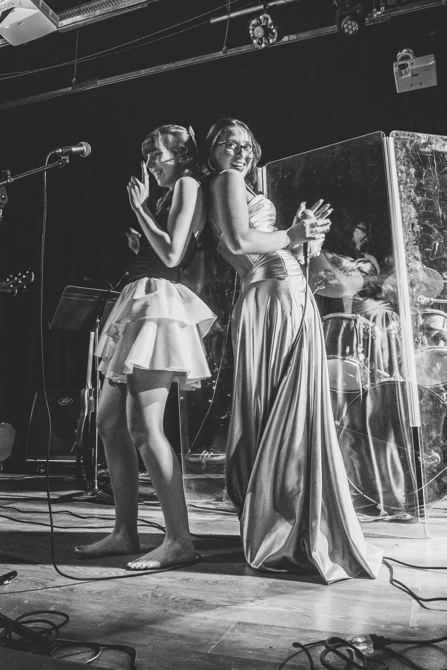 Two women performing on stage in elegant dresses, singing into microphones at a live music event.