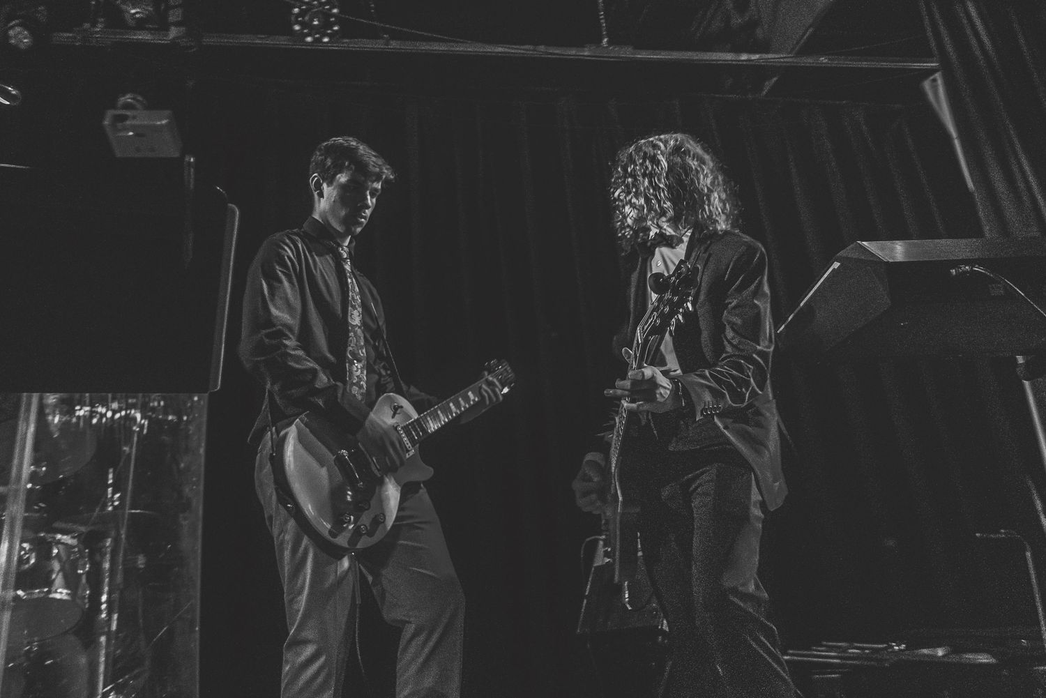 Two guitarists performing on stage together in moody black and white concert photo.