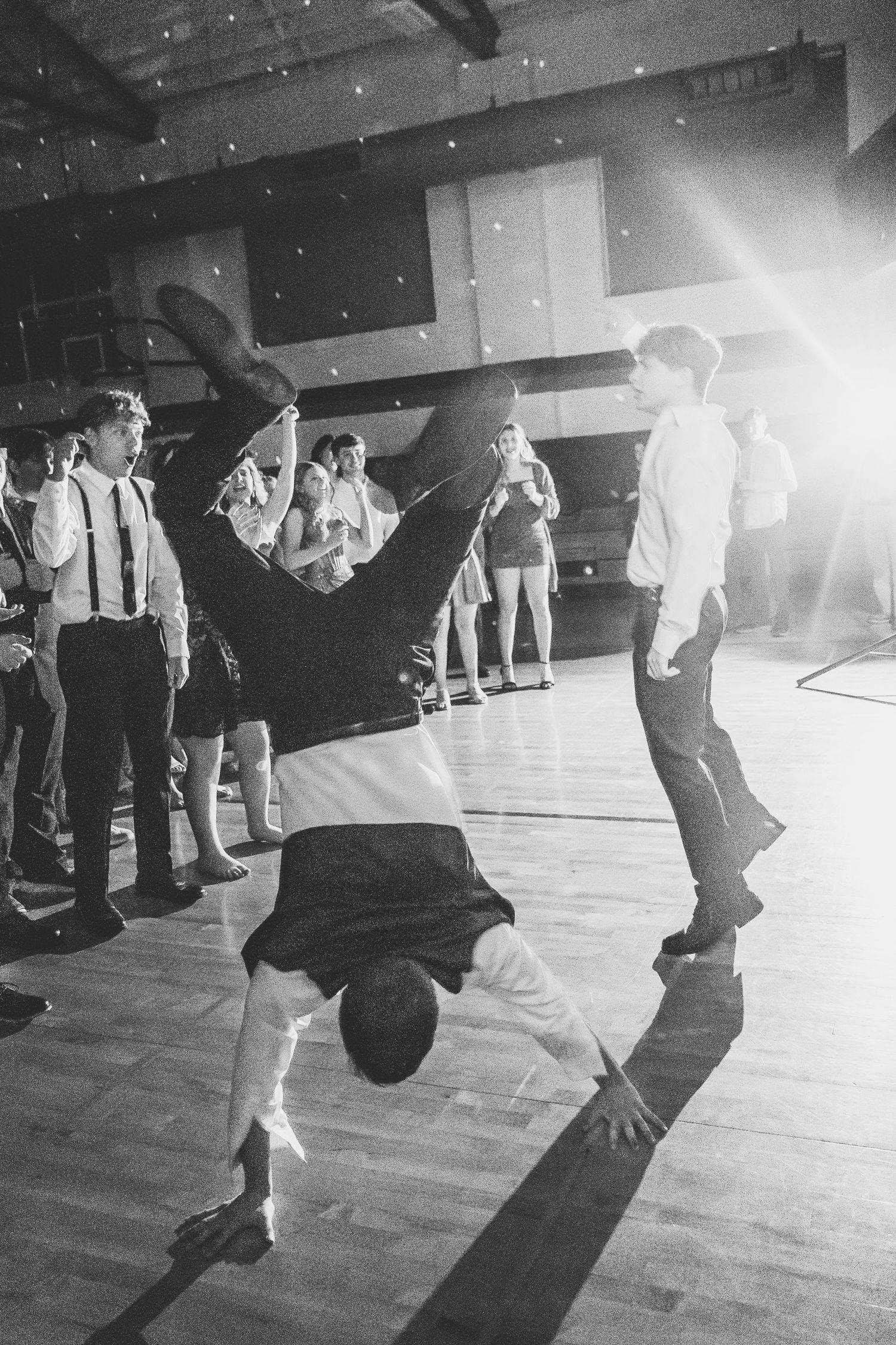 Black and white photo of a person doing a handstand on a dance floor at a formal event.