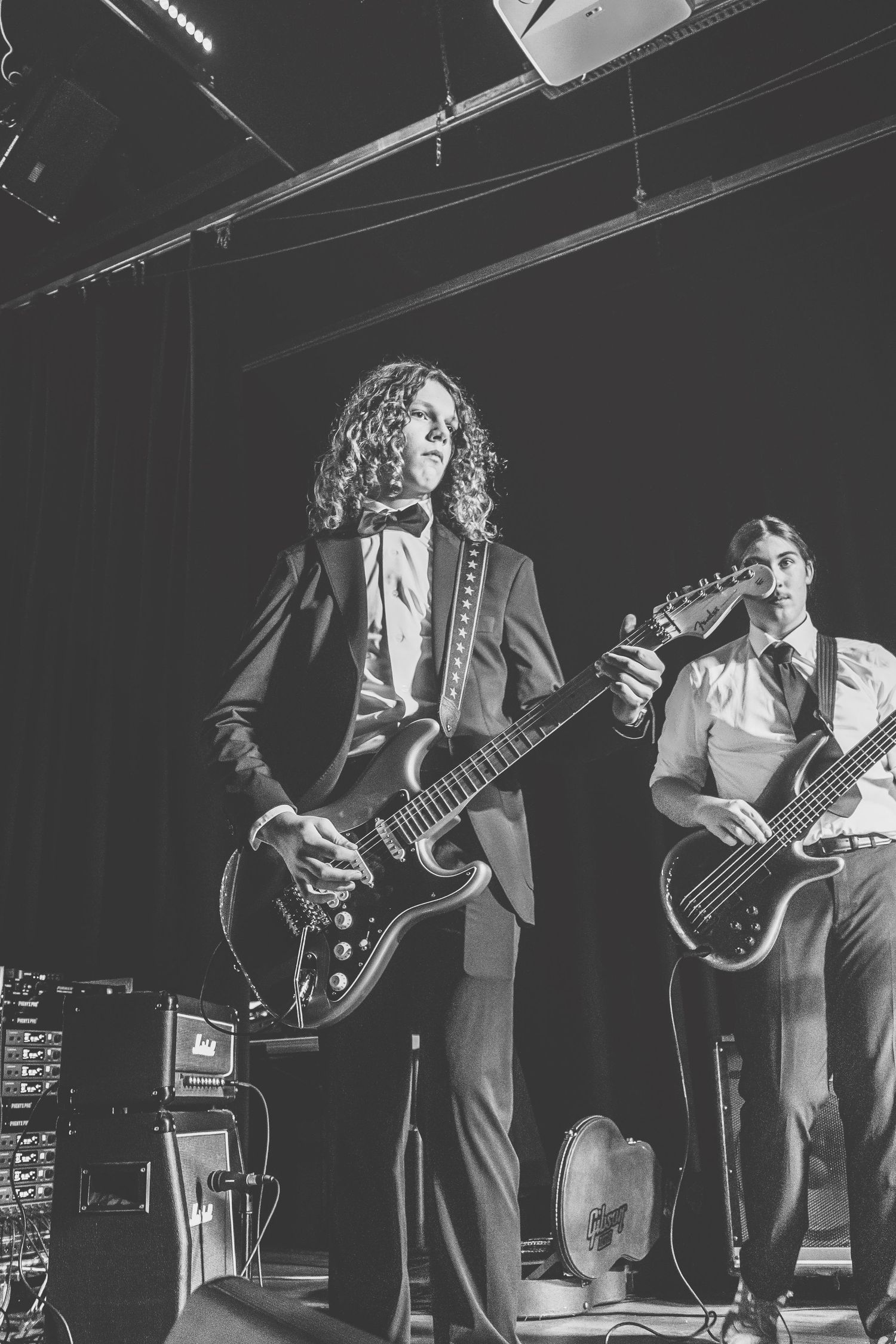 Two guitarists perform on stage in formal attire at a live music event in black and white.
