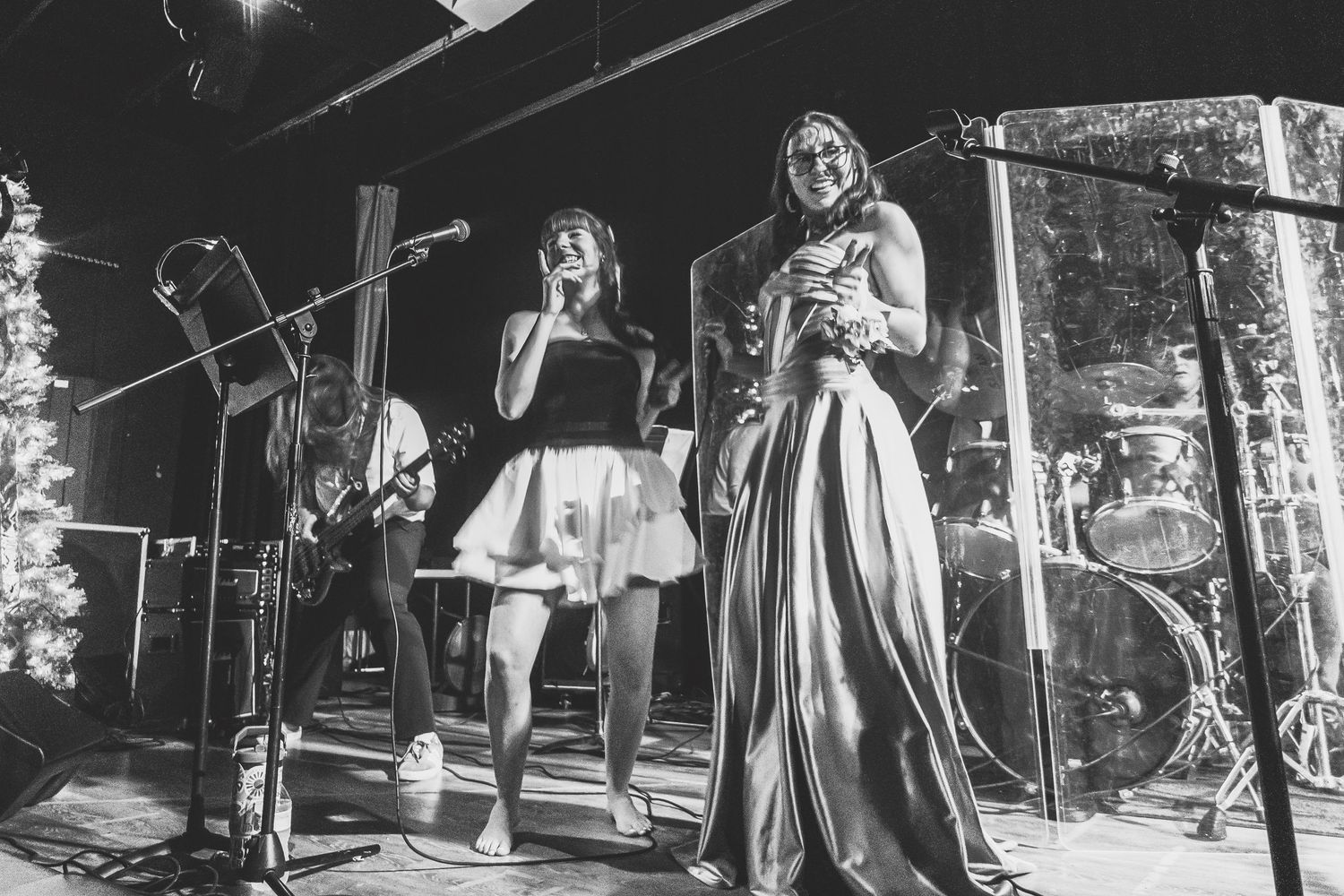 Two female vocalists perform on stage with a band at a live music event in black and white.
