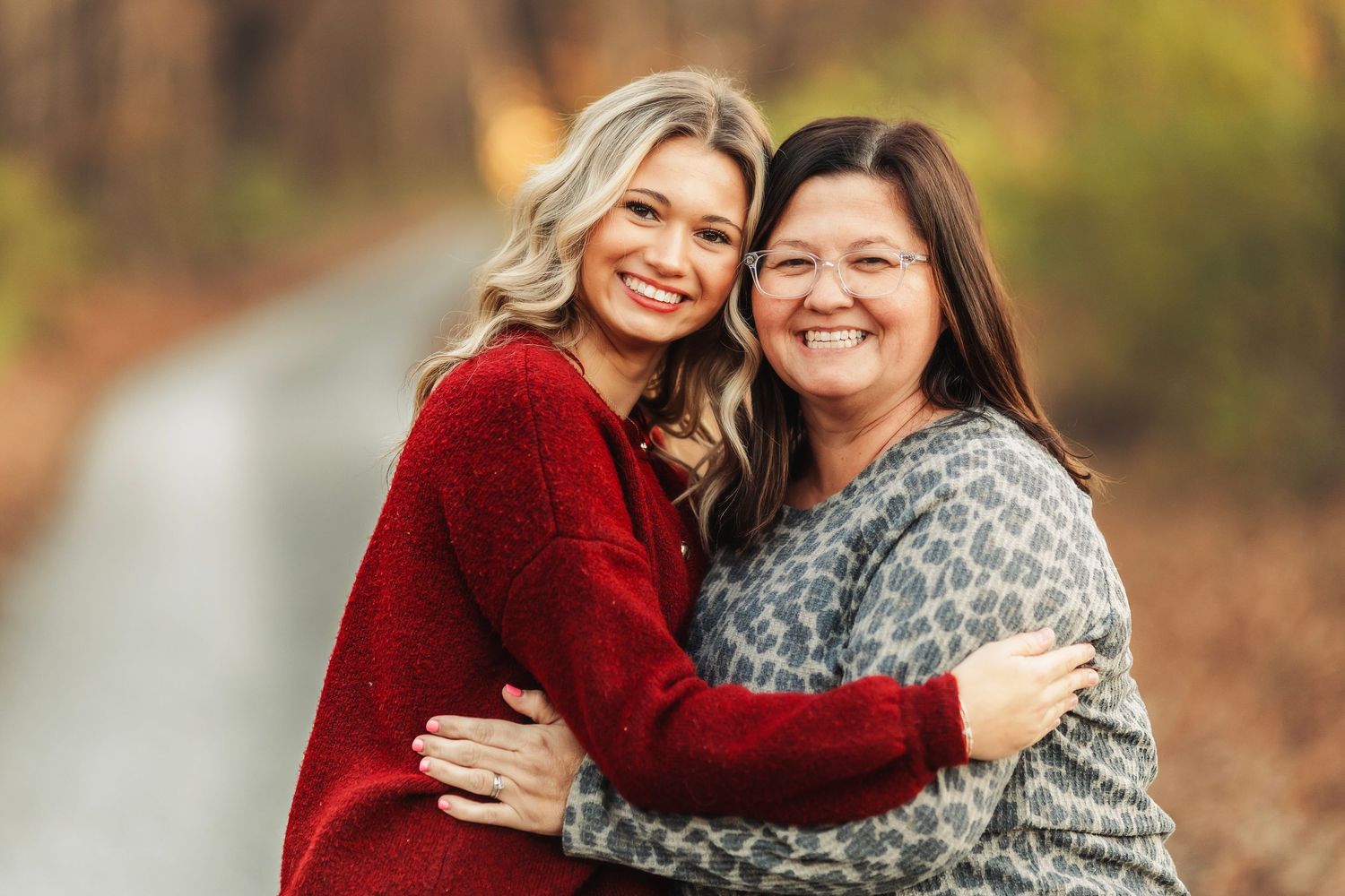 Two people in red and gray sweaters embrace while smiling outdoors during autumn.