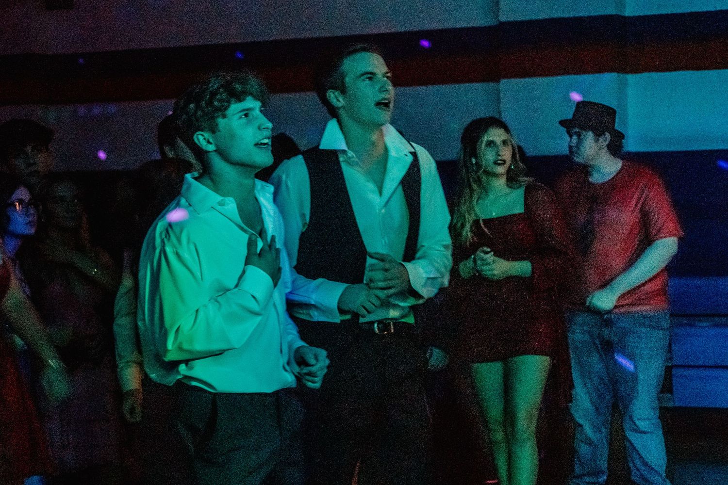 Group of young adults at a dimly lit party, dressed in stylish outfits under colorful neon lights.