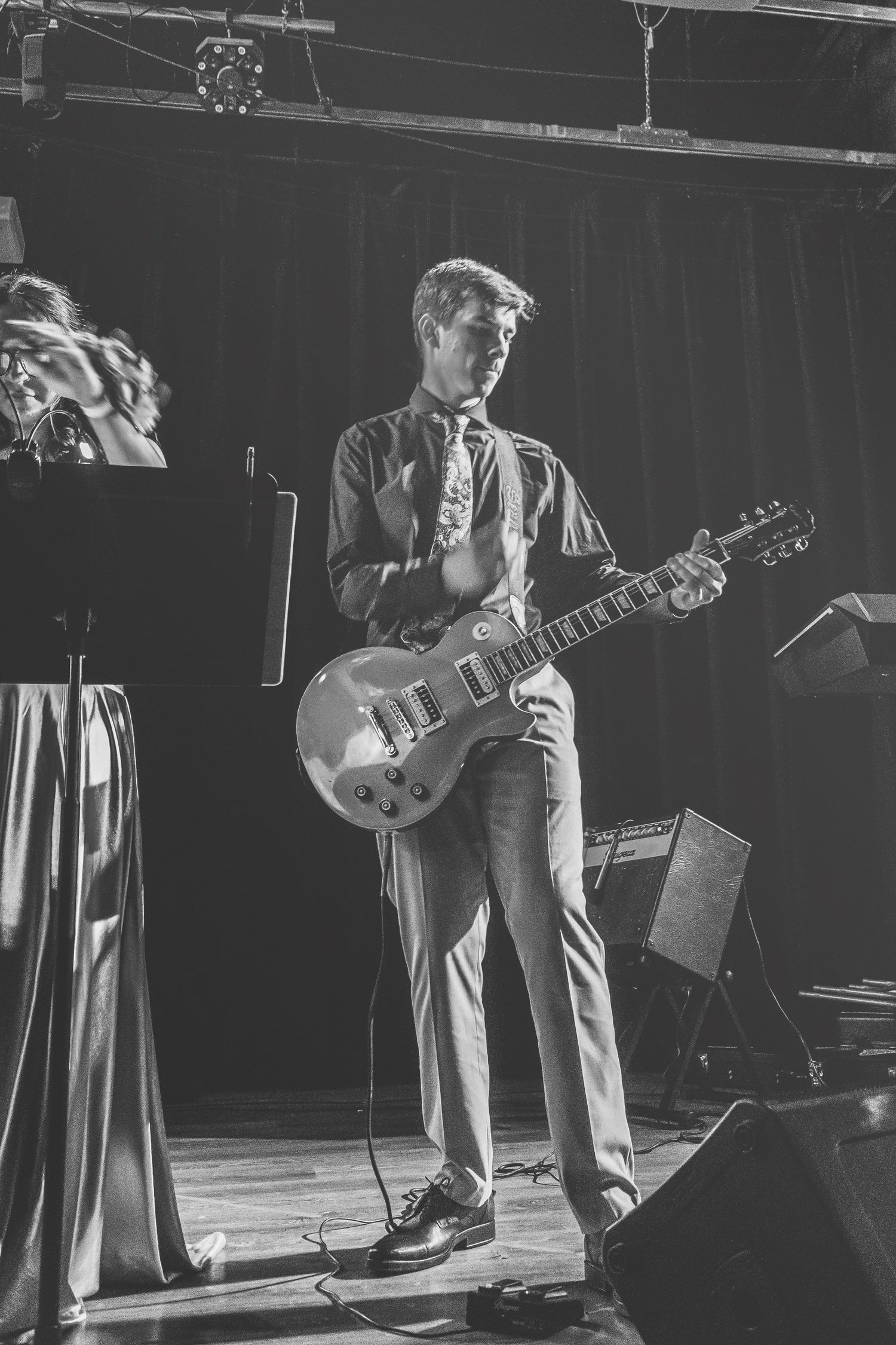 Black and white photo of a male guitarist playing a Les Paul guitar on stage during a live performance.