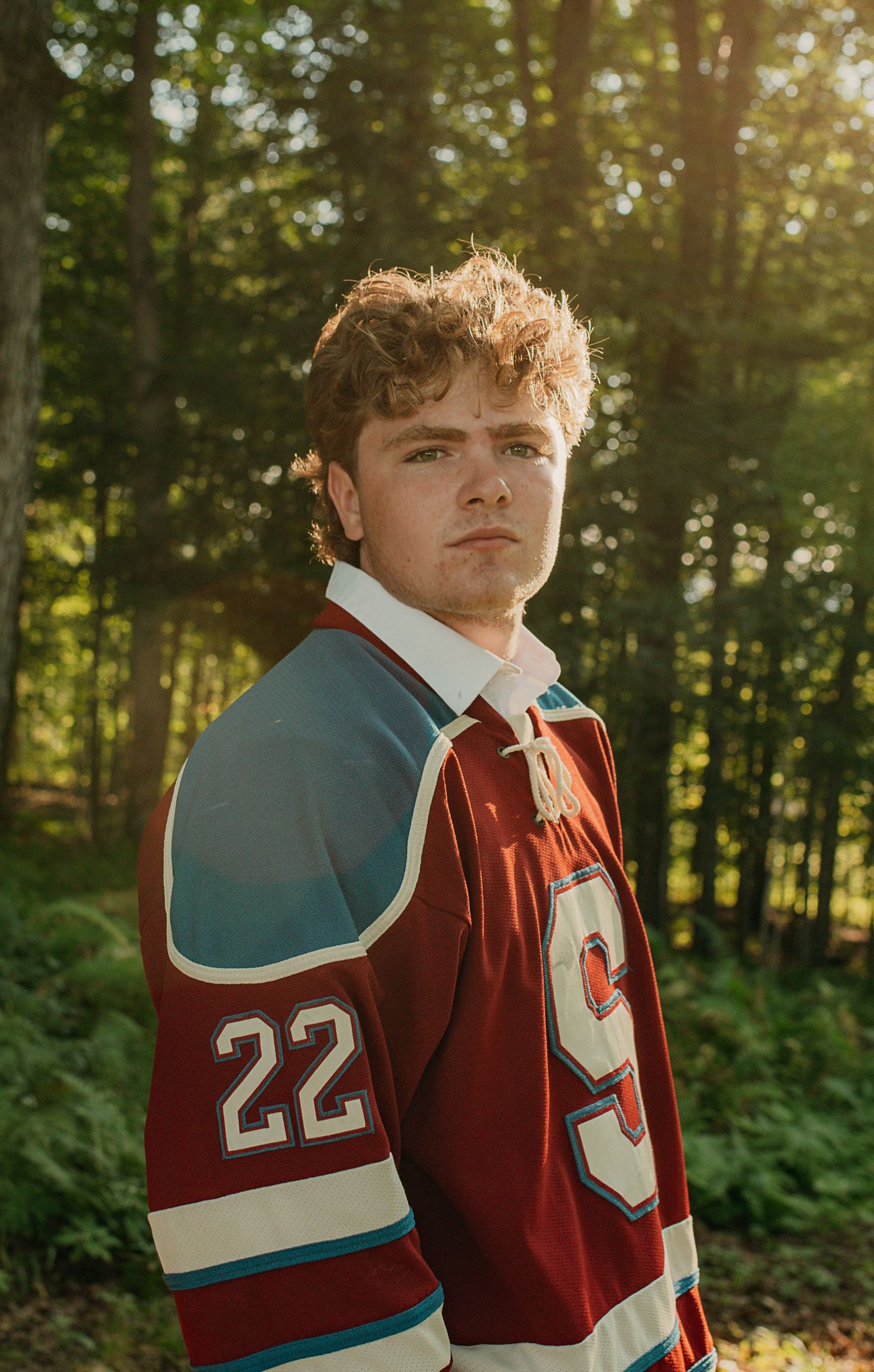 Athlete poses in red and teal sports jersey number 22 in woodland setting.