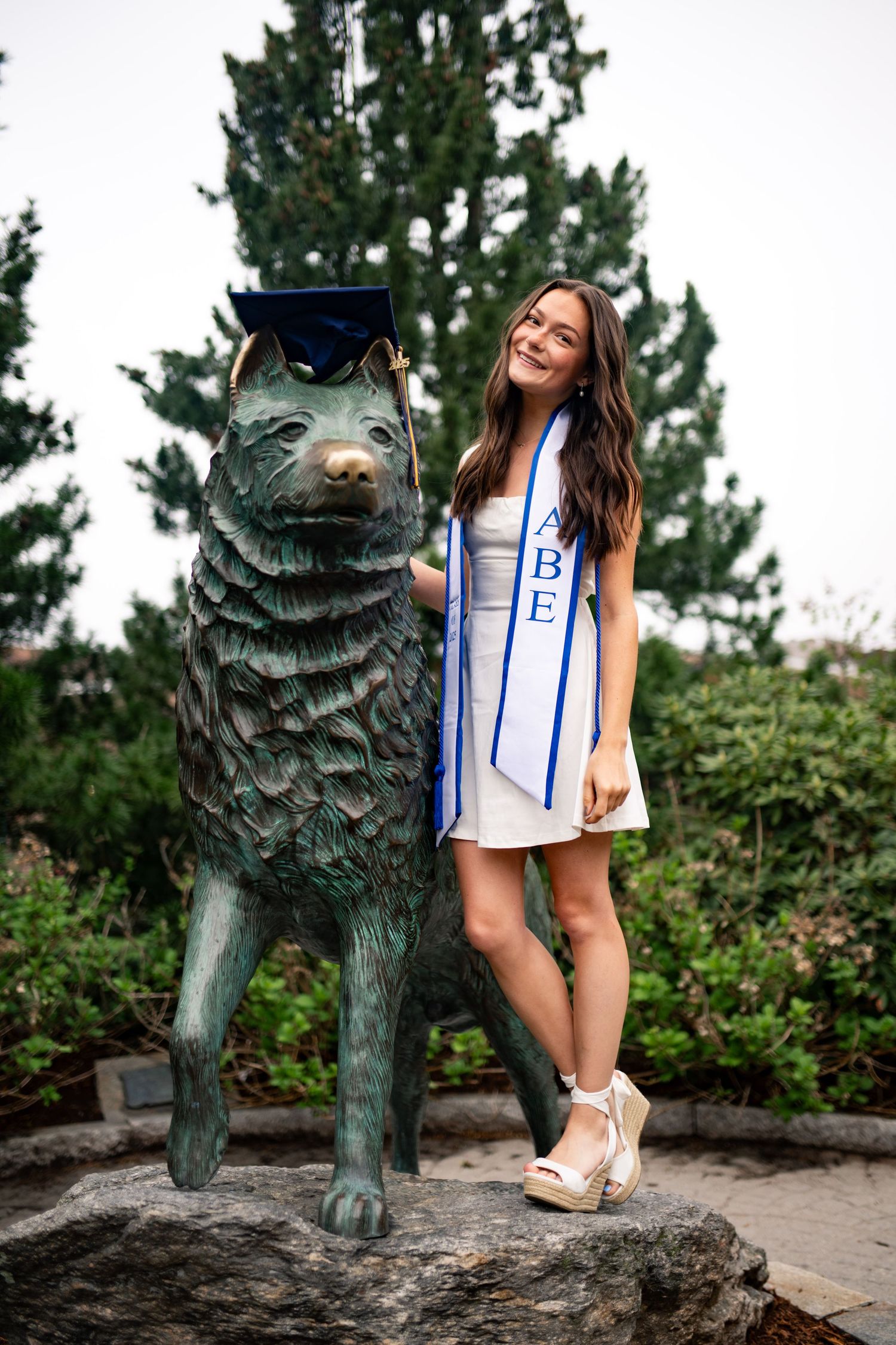 Person wearing a blue and white sports jersey poses playfully with a decorative bronze wolf statue in an outdoor setting.