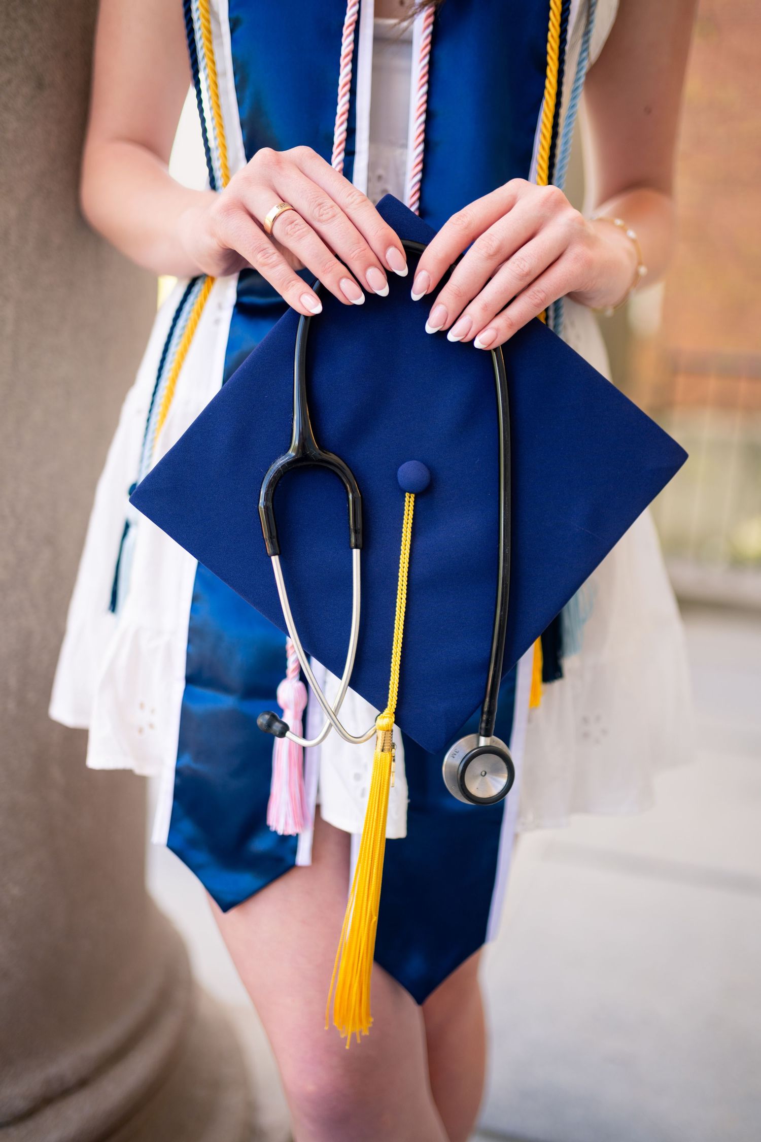 Medical graduate holding graduation cap and stethoscope with blue regalia and yellow tassel for graduation photos.