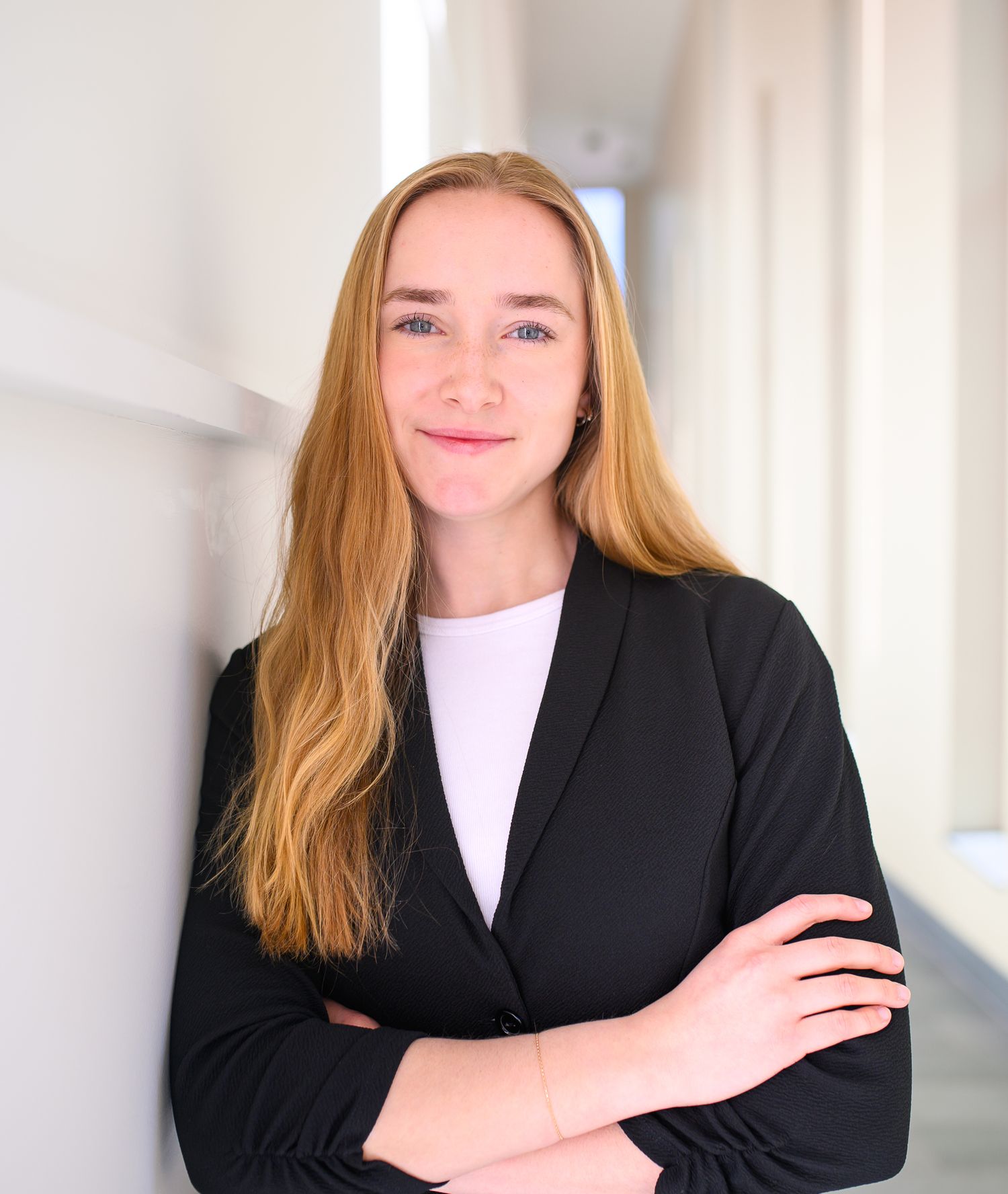 Professional portrait of someone in a black blazer and white shirt against a light background.