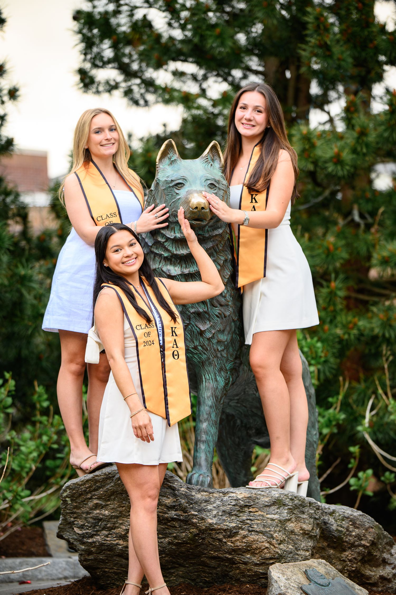 Three Alpha Xi Delta sorority sisters pose with university mascot statue on rocks in outdoor setting.