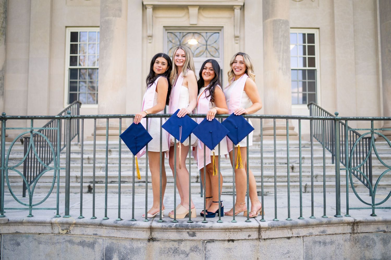 A group of people stand on a grand stone balcony wearing white outfits and taking photos in bright daylight.