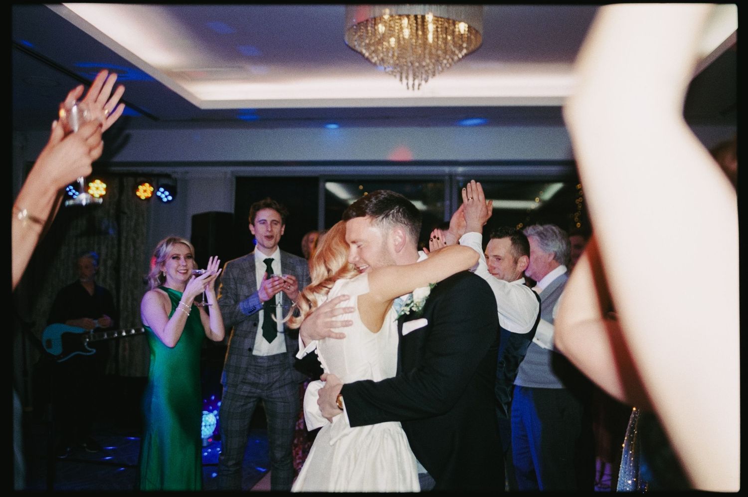 Bride and groom share a romantic first dance kiss surrounded by cheering guests at elegant wedding reception.