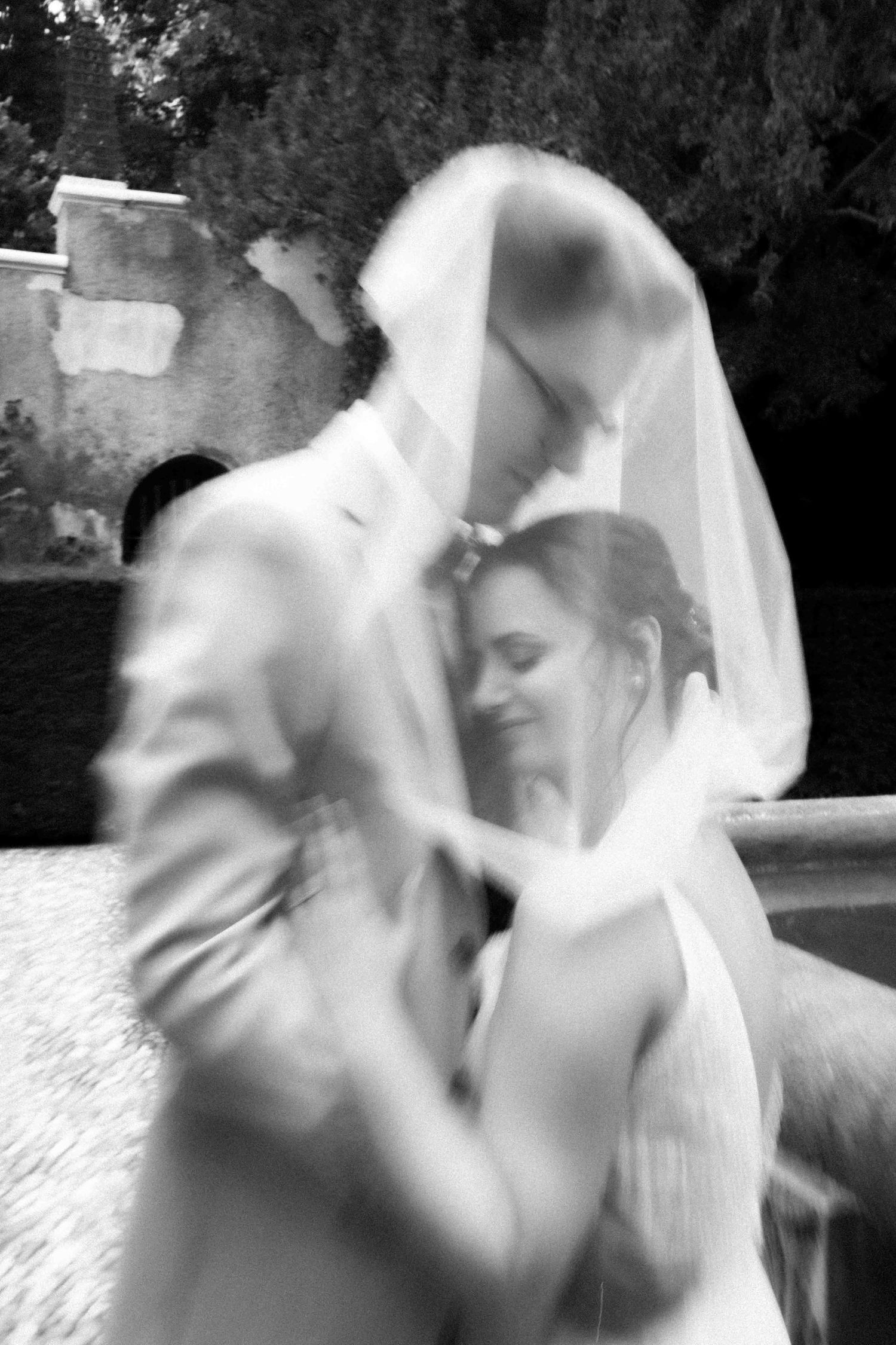 Artistic black and white photo of wedding couple embracing with flowing veil movement.