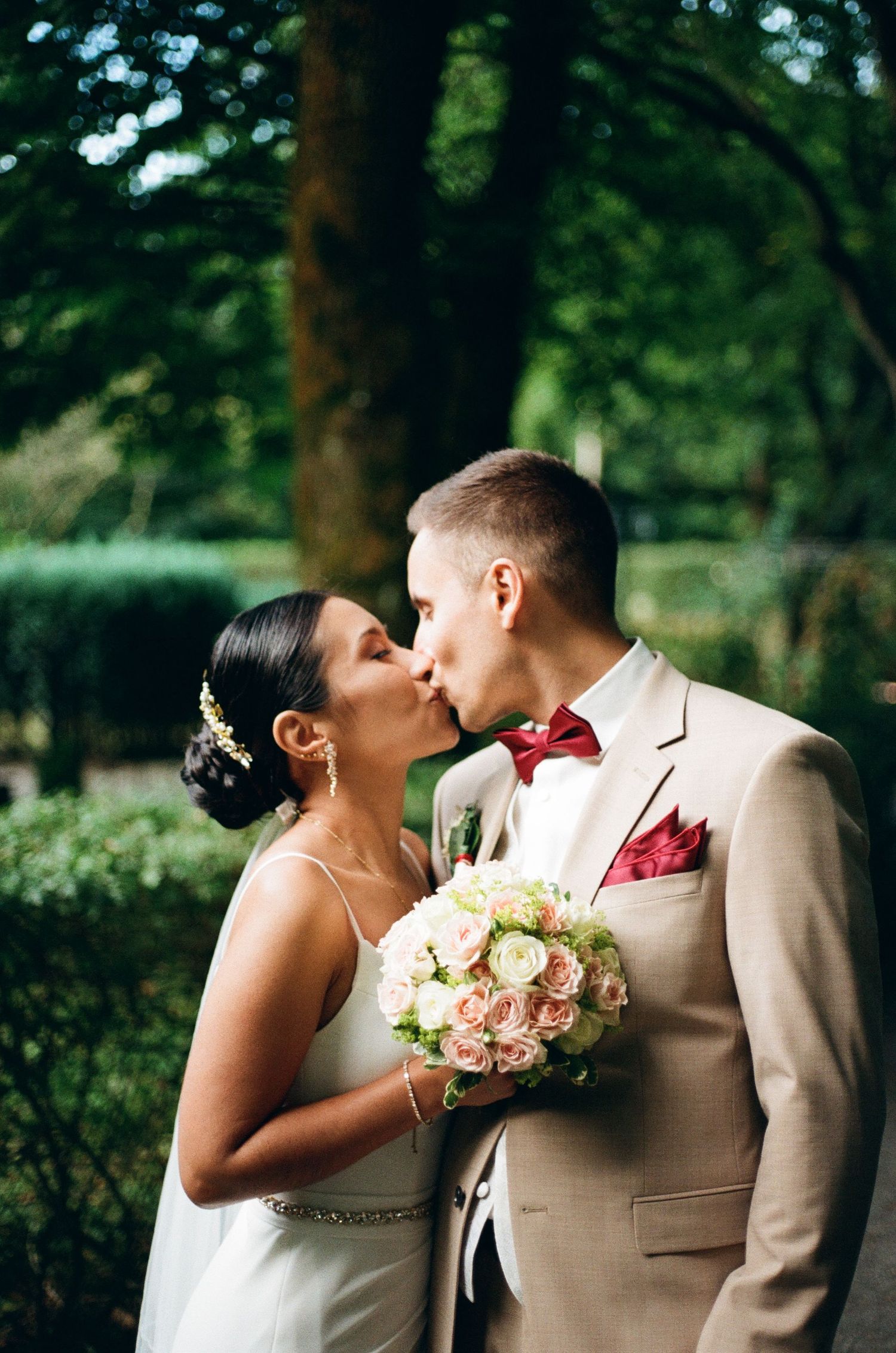 Newlyweds share a romantic moment in a garden setting with pink and white floral bouquet.