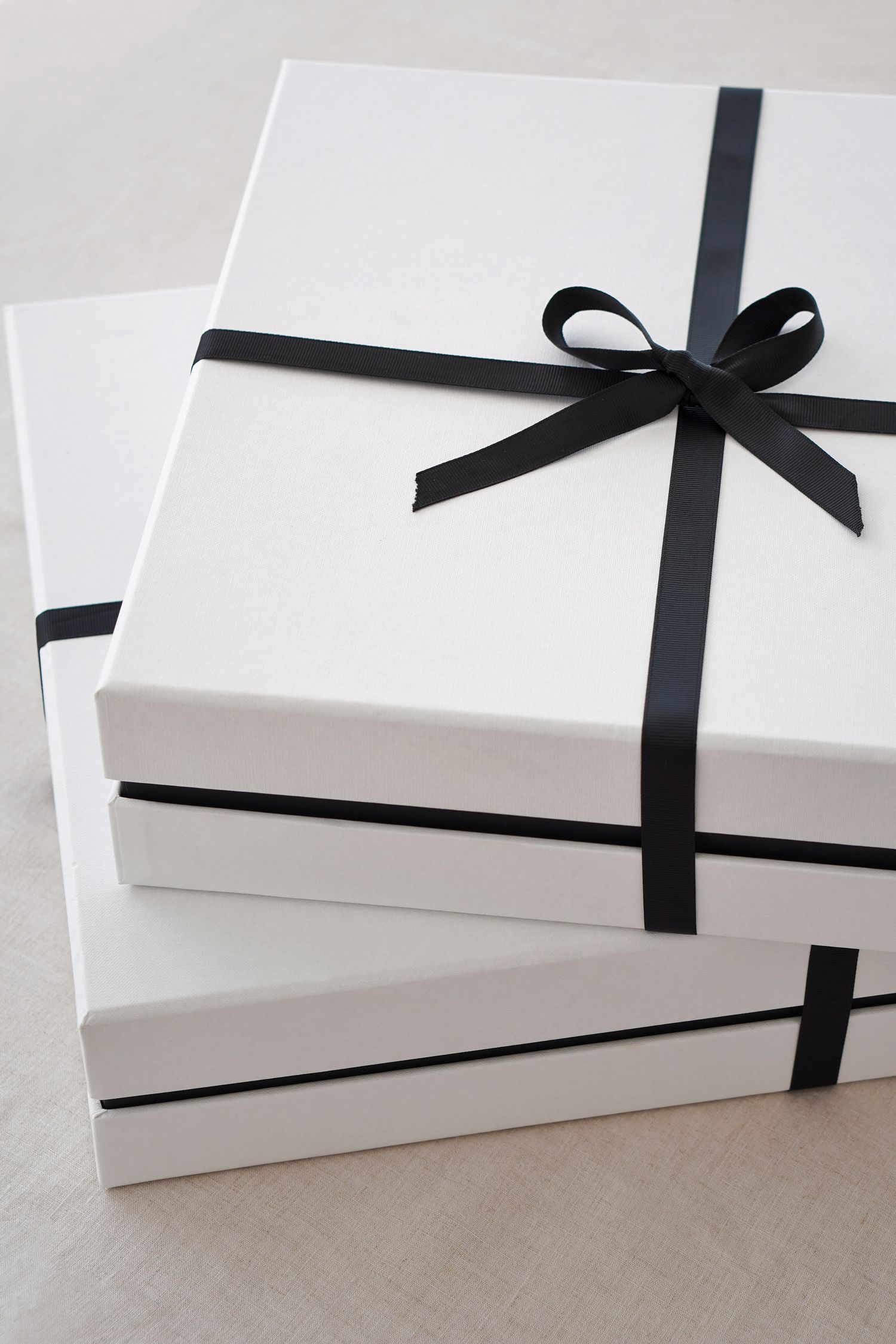 Stack of elegant white gift boxes with black ribbon bows for minimal and sophisticated gift presentation.