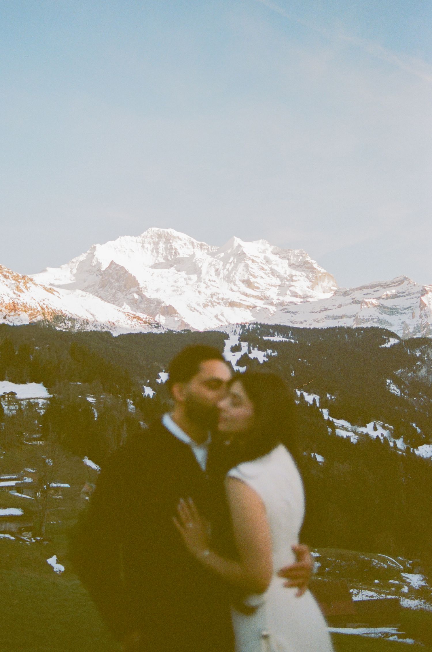 Couple sharing a romantic kiss with snow-capped Swiss Alps mountains in the background during their winter wedding.