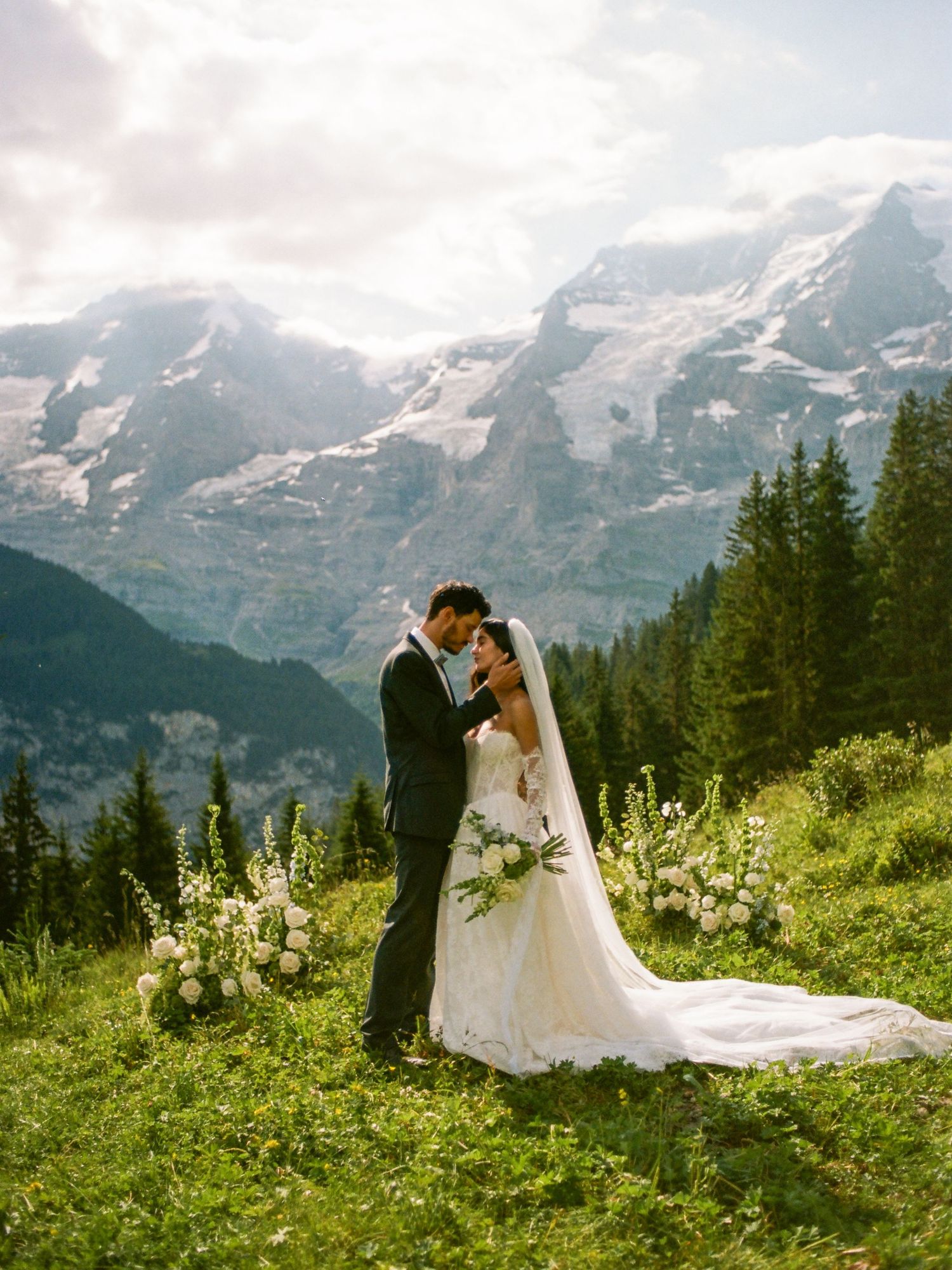 Bride and groom share a romantic moment on a Swiss alpine meadow with stunning snow-capped mountain peaks backdrop.