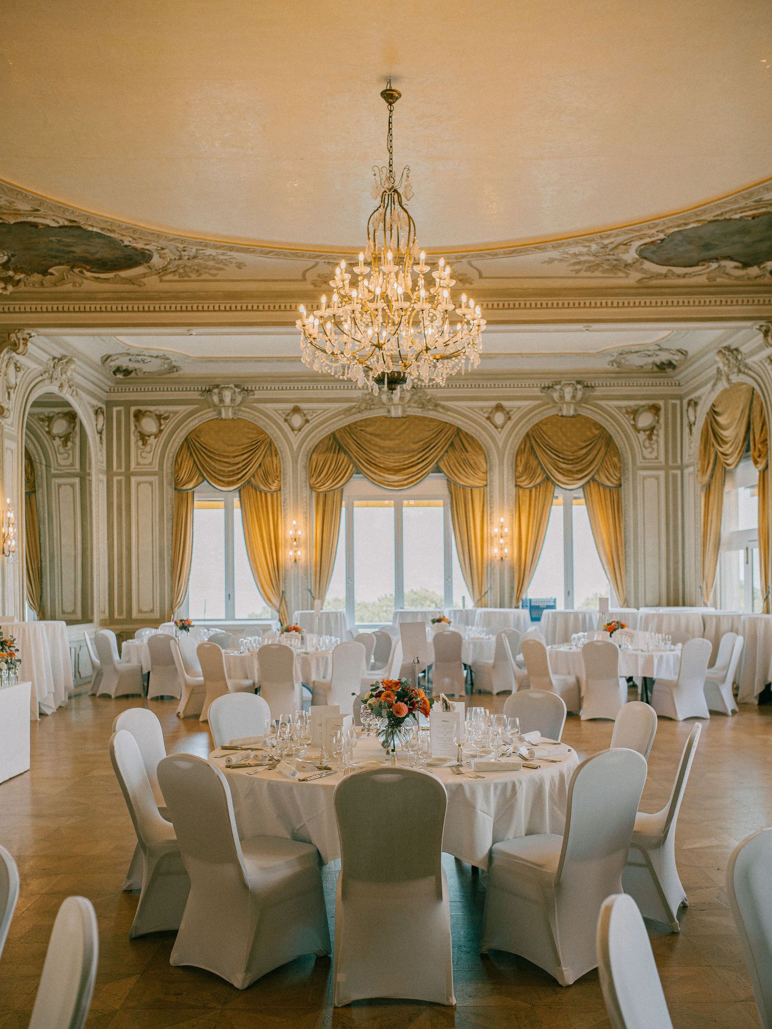 Elegant ballroom with crystal chandelier and round tables set for a formal wedding reception.