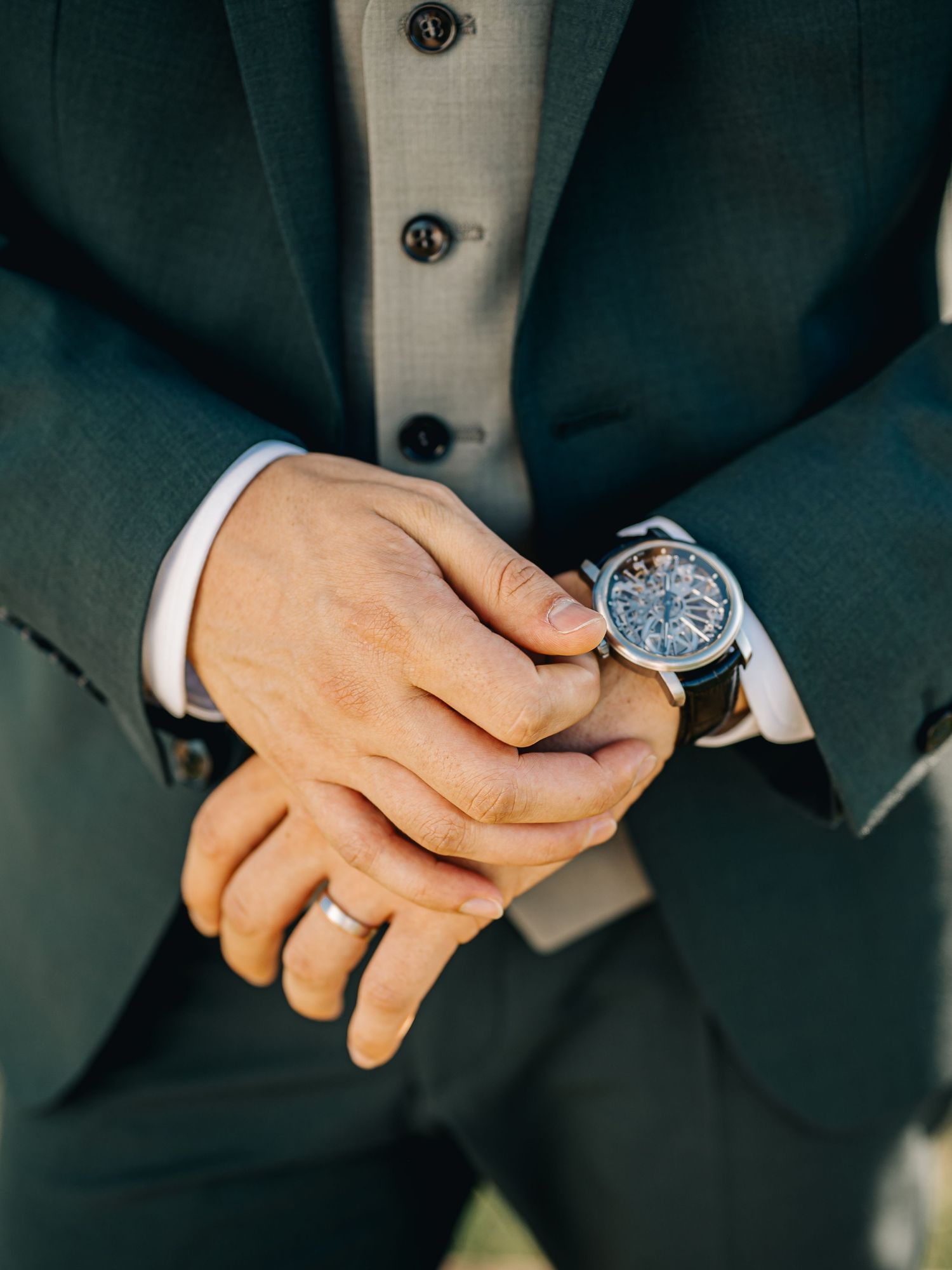 Detail shot of hands adjusting an elegant watch with wedding band visible.