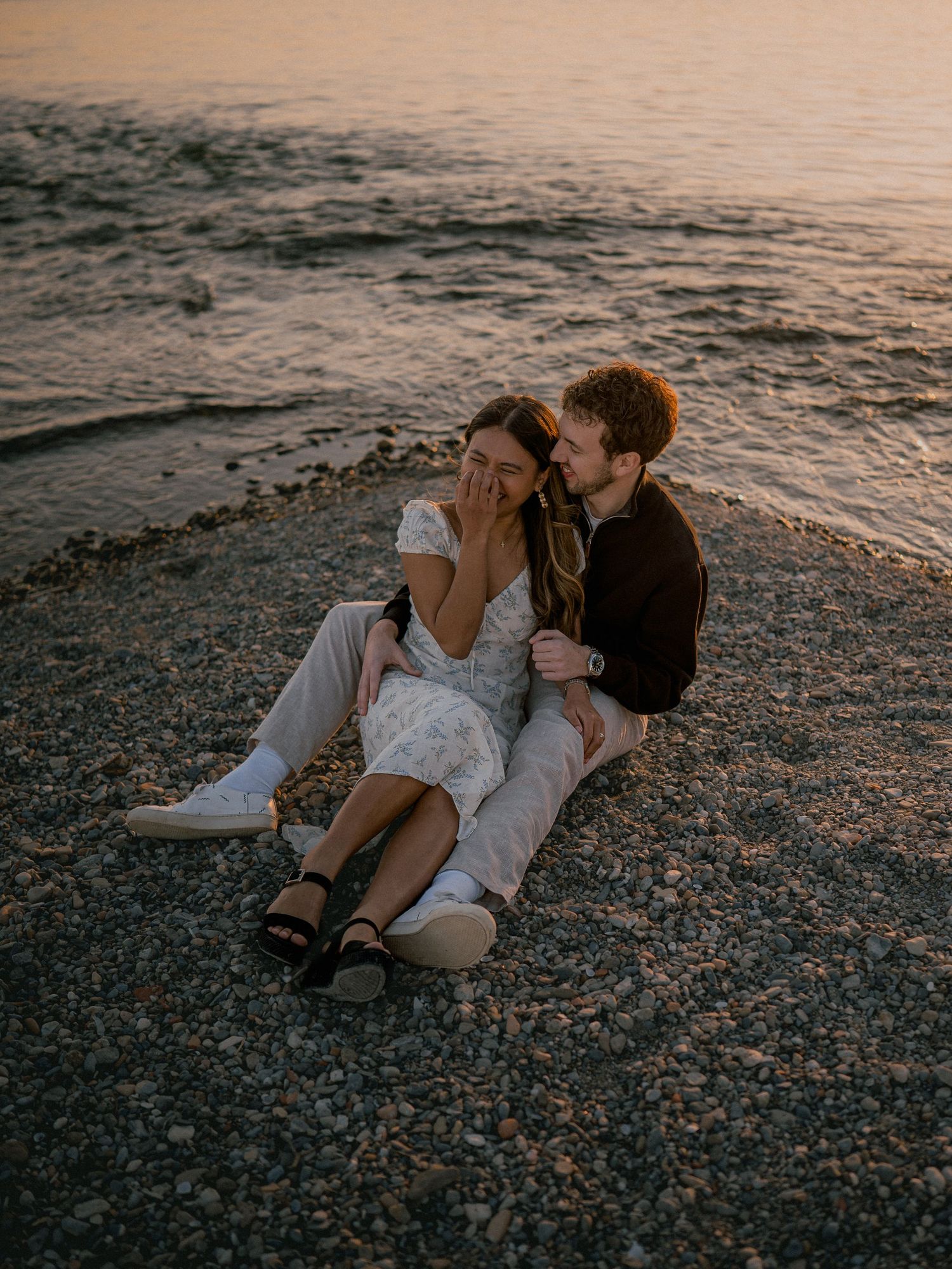 Romantic couple embraces on rocky beach at sunset creating intimate silhouettes against golden water.