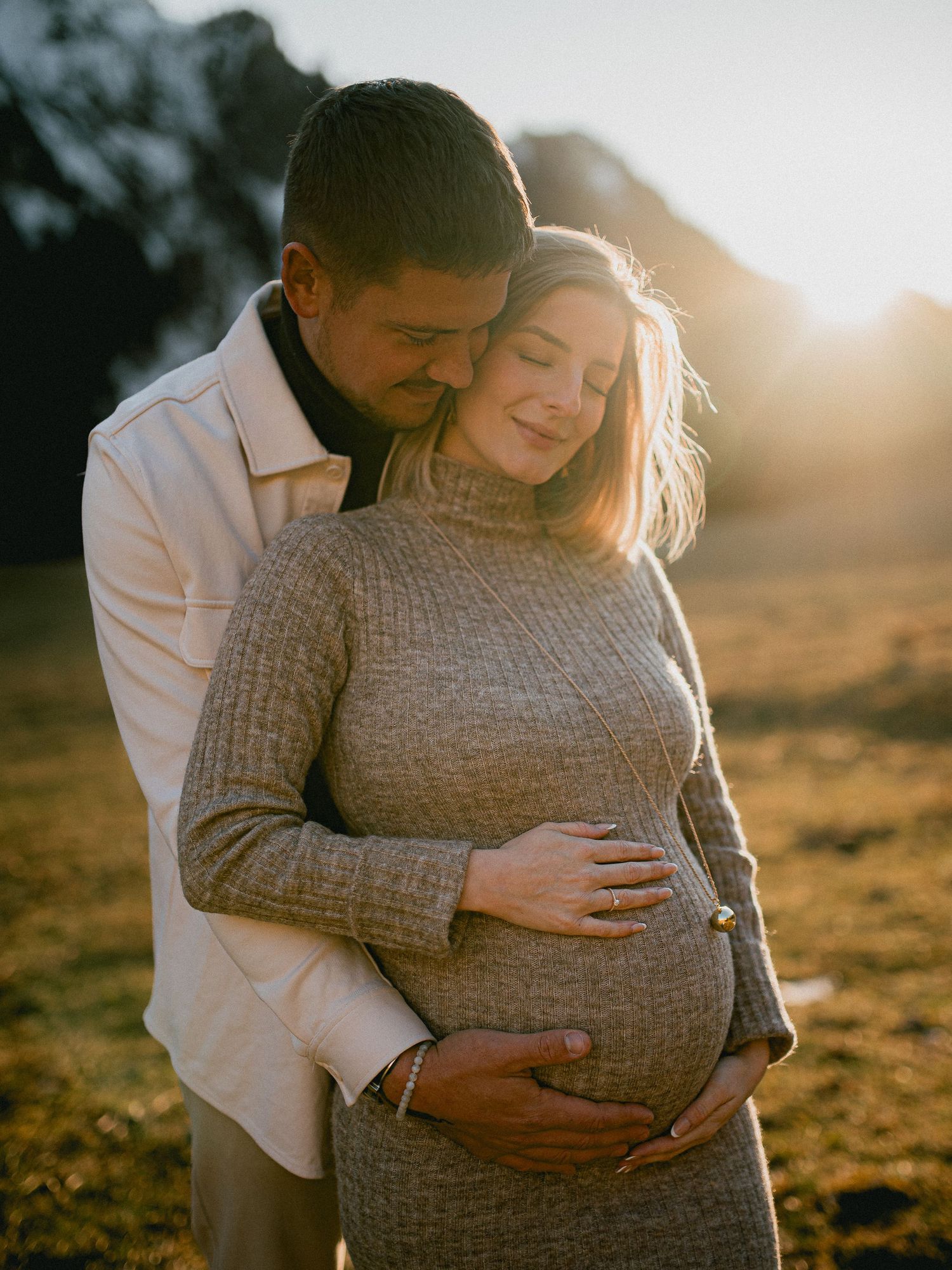 A couple embraces during golden hour maternity photoshoot in a desert landscape setting.