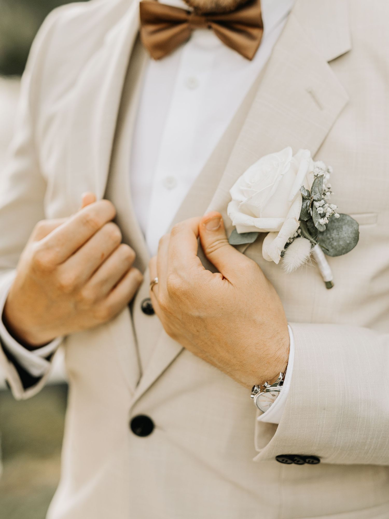 Close-up details of groom's white tuxedo jacket with brown bowtie.