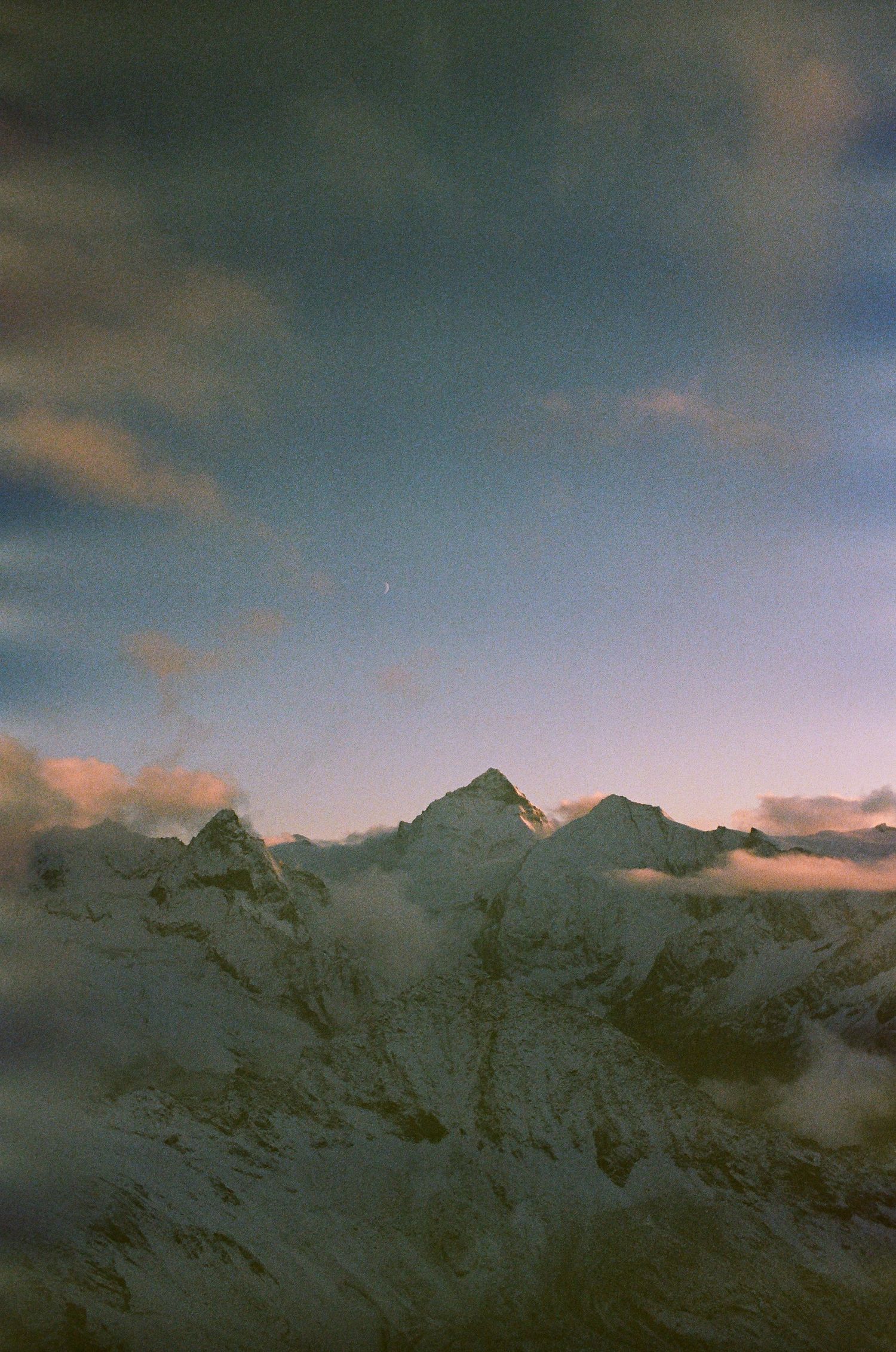 Snow-capped mountain range under pink-tinged clouds at dusk.