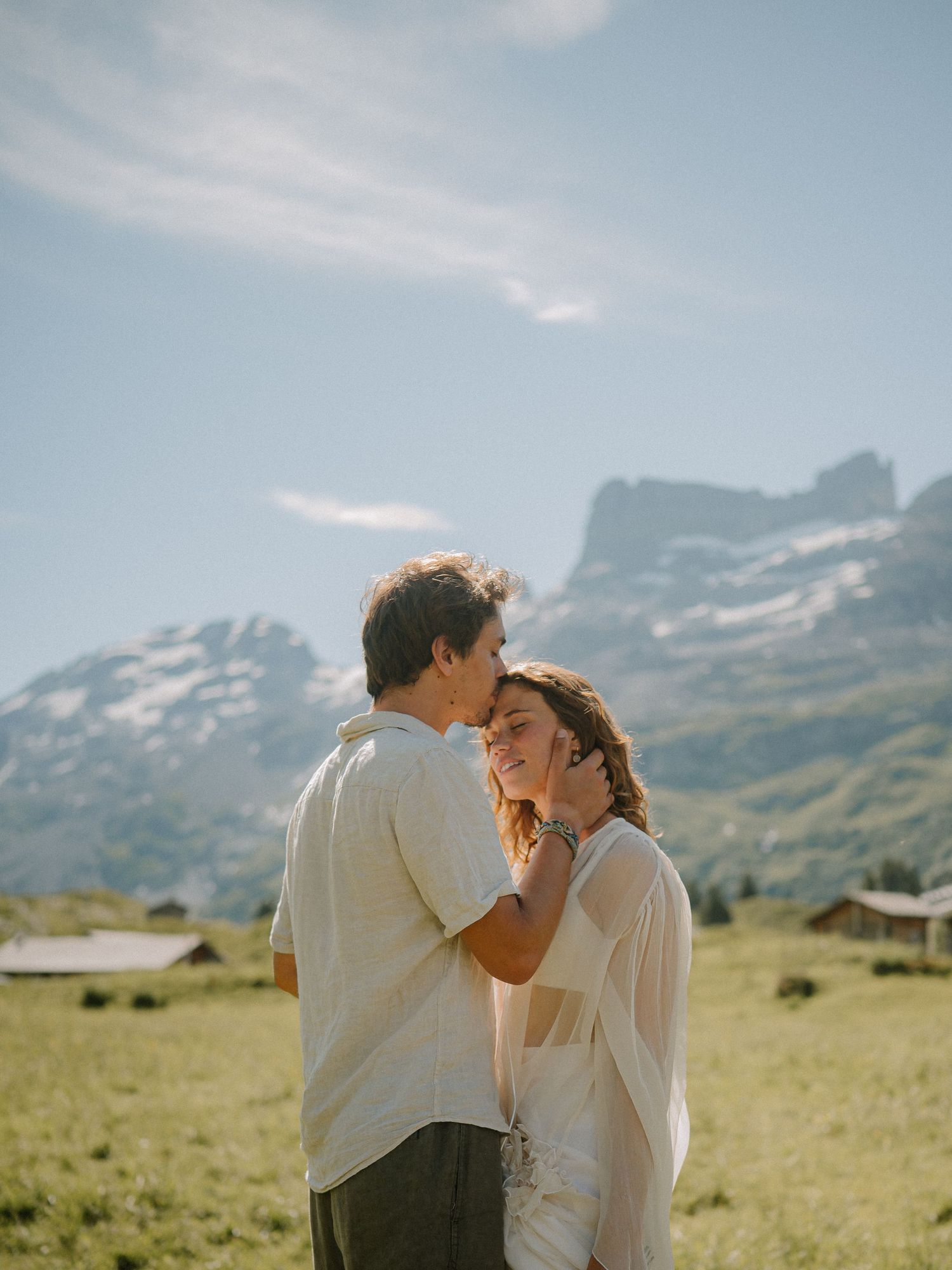 A couple sharing a tender moment in a mountain meadow with scenic views.