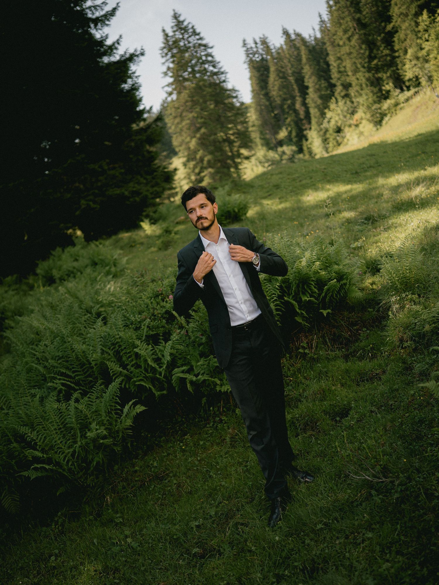 Person in formal attire walking through a fern-filled forest setting.