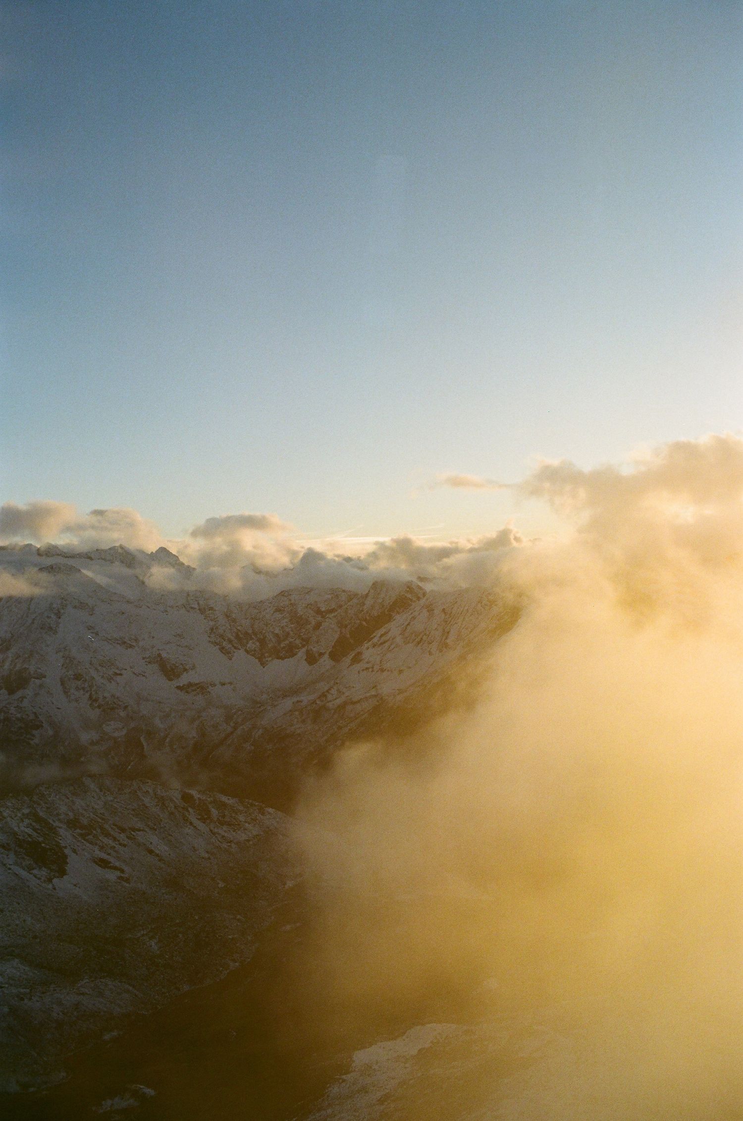 Golden sunlight illuminates mountain valley with dramatic fog and clear sky above.