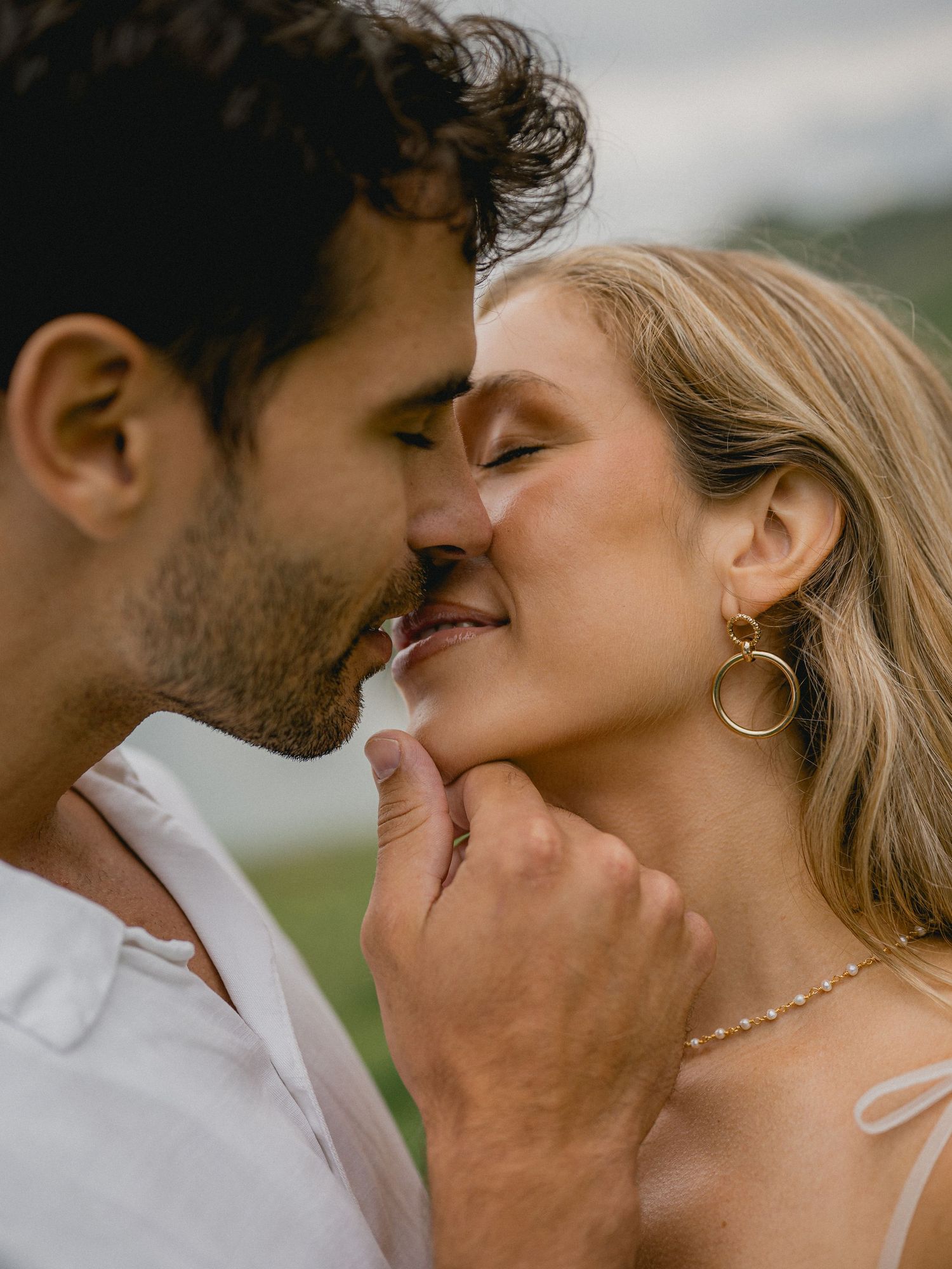 A romantic close-up of a couple sharing an intimate moment in a sun-lit outdoor setting.