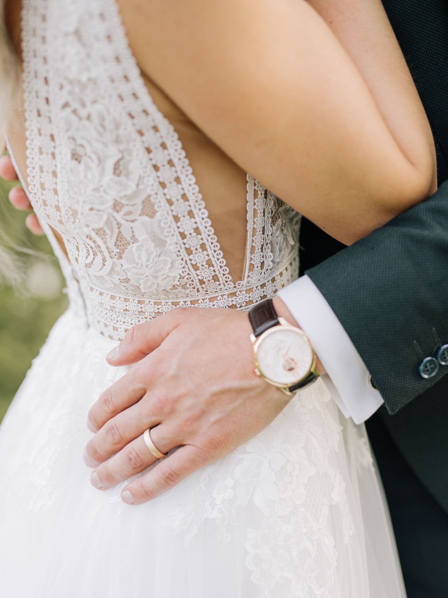 Close-up detail of a beaded wedding dress bodice with lace and a groom's hand on the waist.