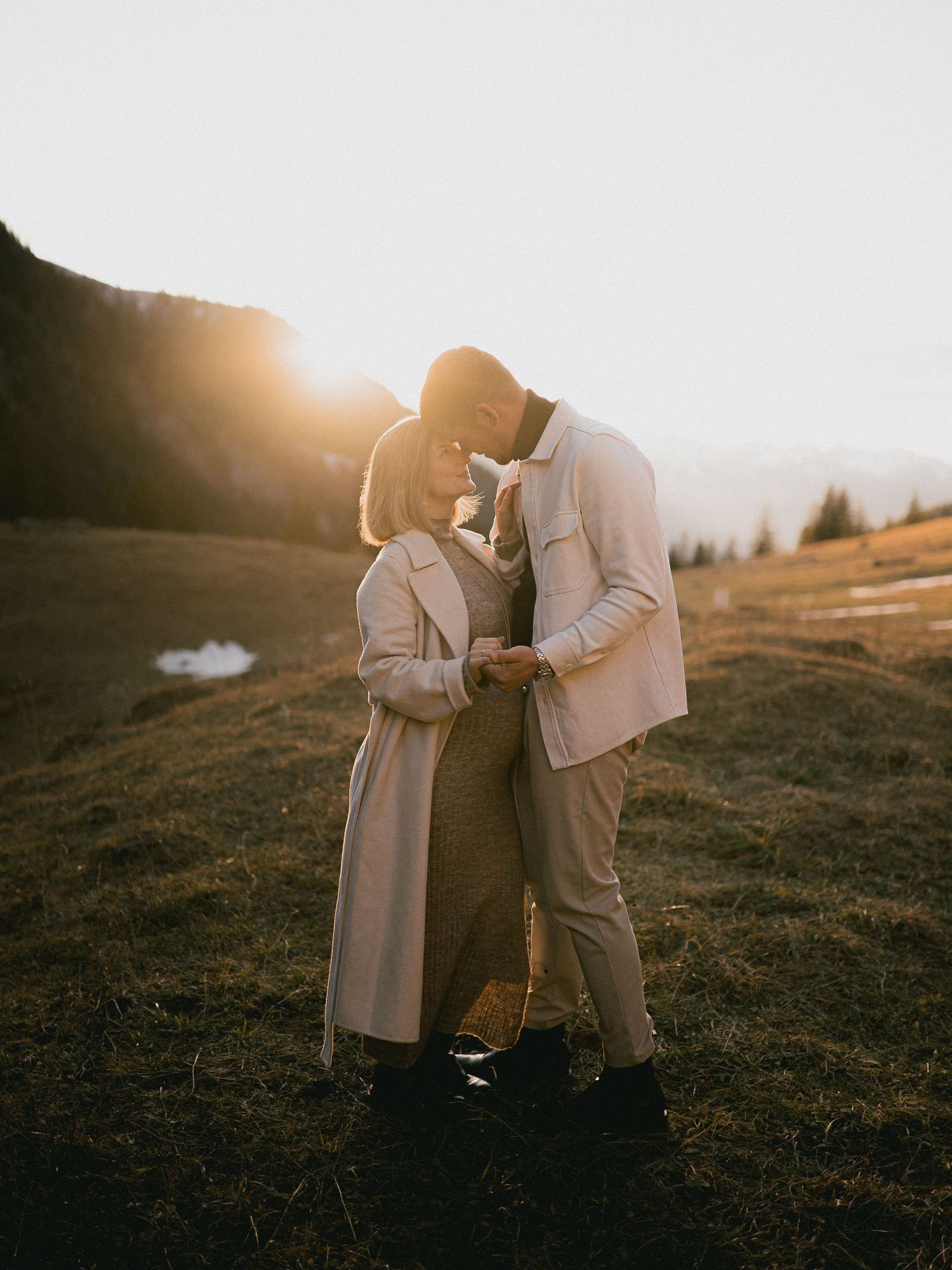 A couple shares a romantic moment on a hillside at sunset in warm autumn light.
