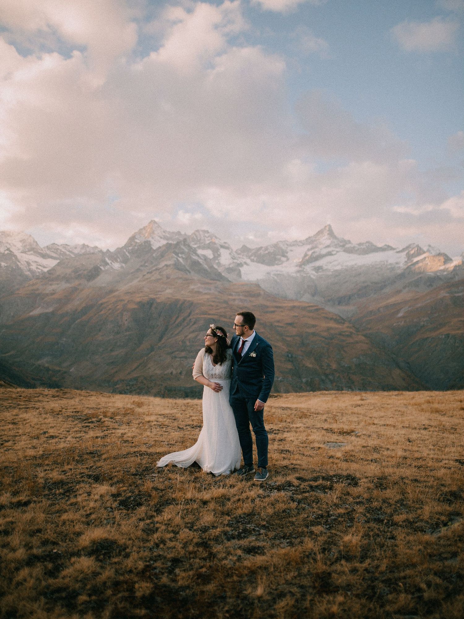 Newlyweds sharing an intimate moment against dramatic mountain landscape.