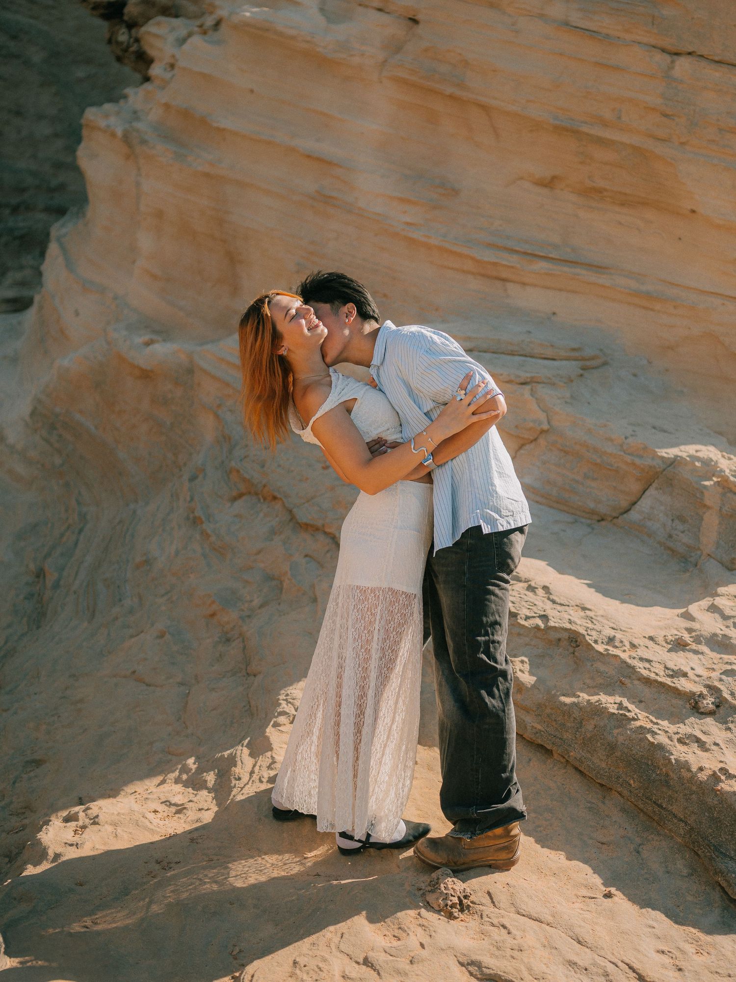 A couple shares a romantic moment against orange sandstone cliffs in a desert landscape.
